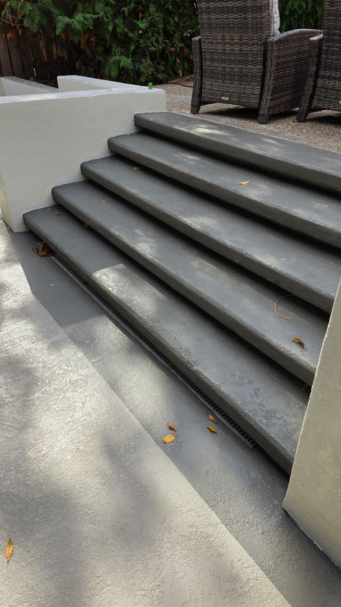 Outdoor concrete steps beside a walkway, with sunlight and a wicker chair at the top.