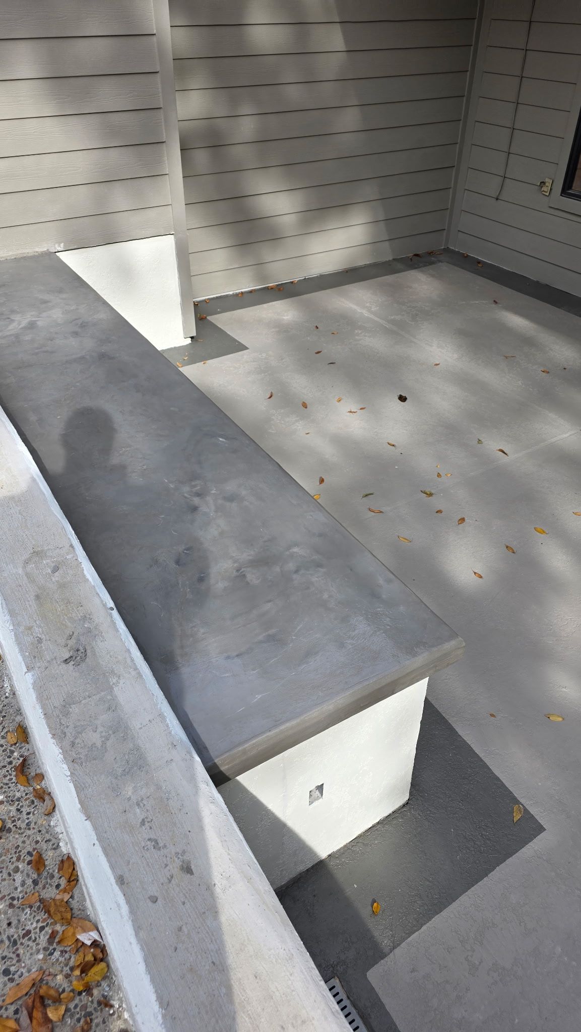 Concrete bench in a small outdoor courtyard with white tiled walls and floor.