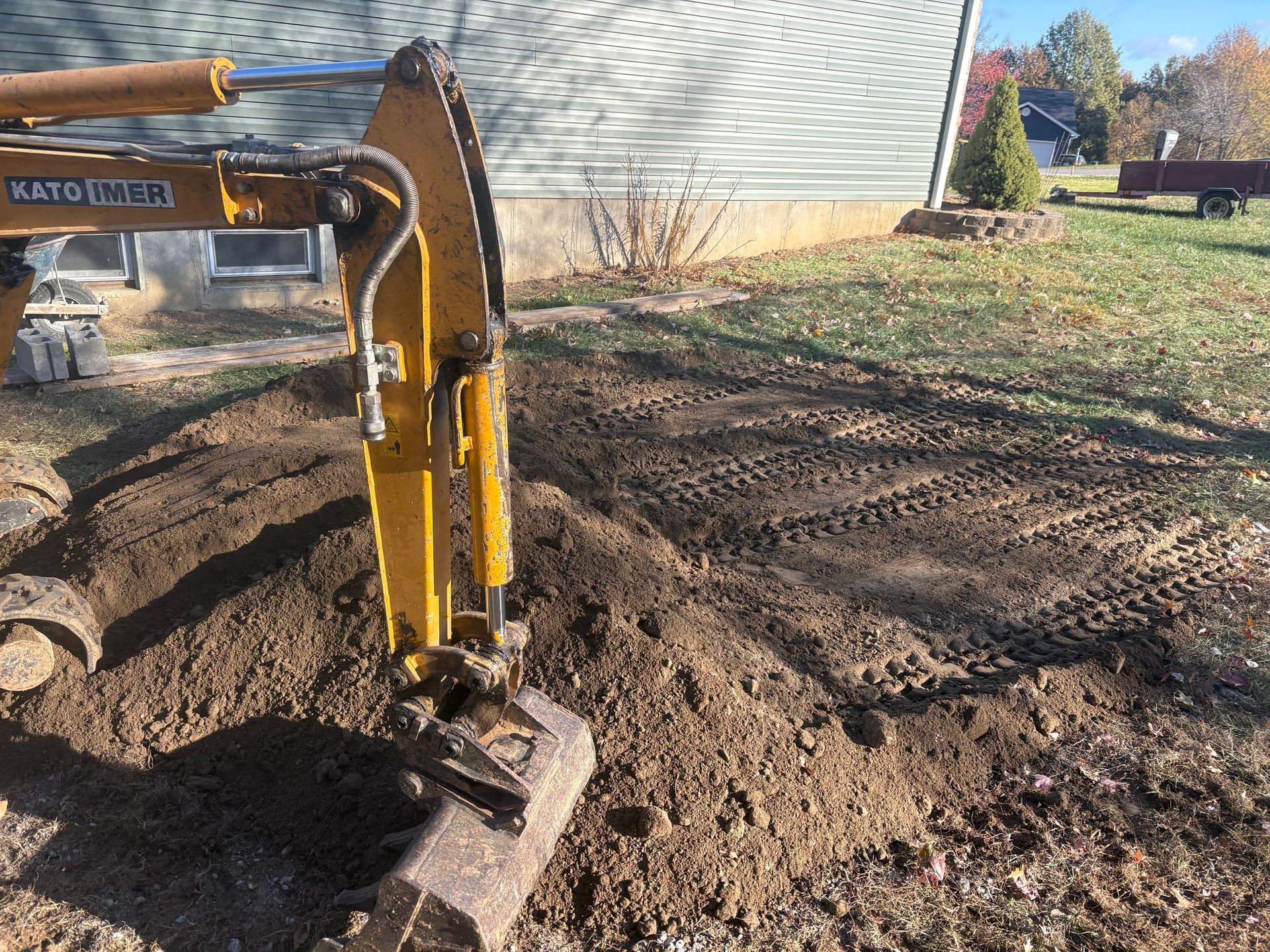 Yellow excavator digging dirt beside a house in a muddy yard.