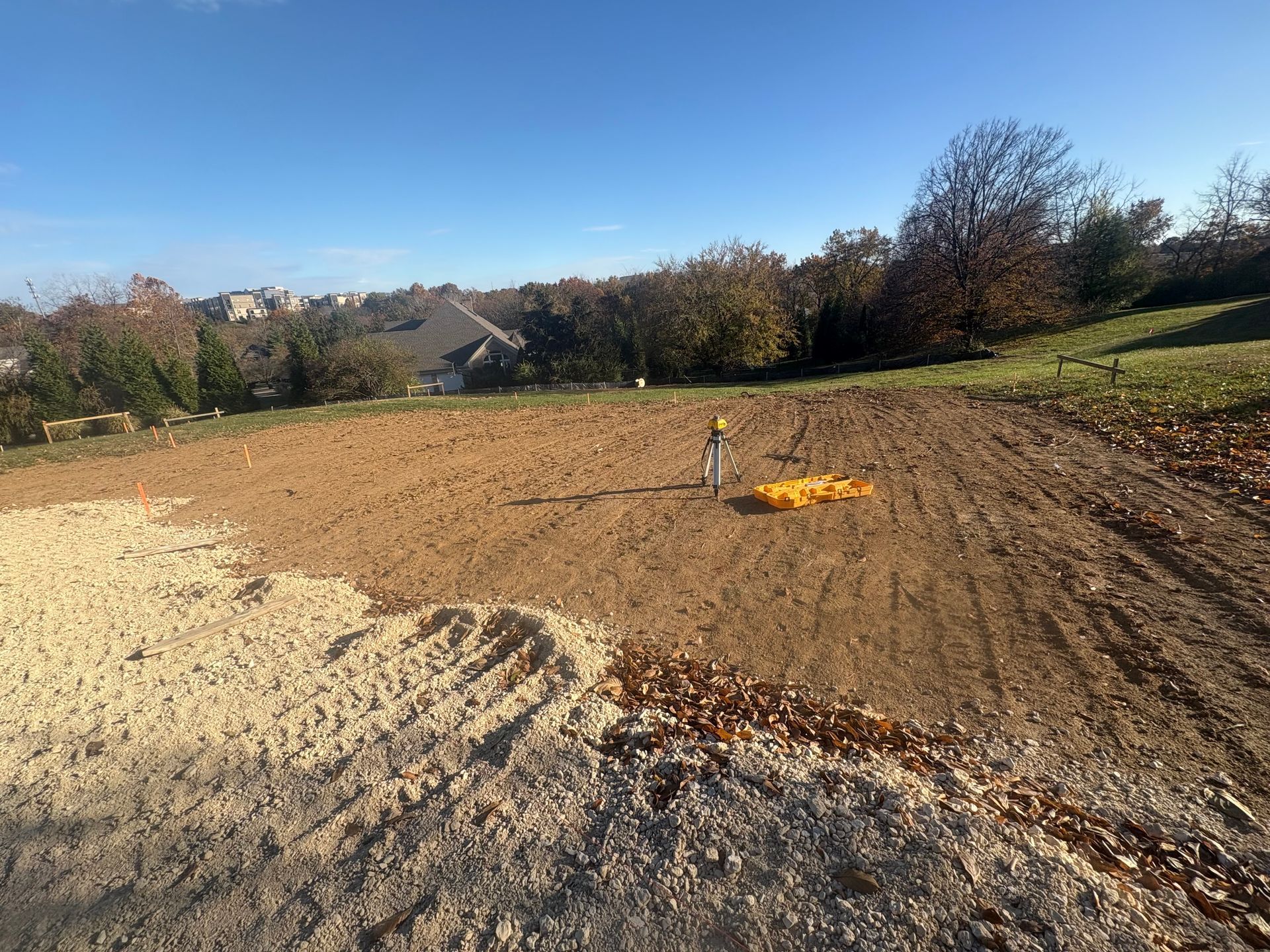 Sandy dirt mound with a small orange tarp in a sunny outdoor field, trees in the background.