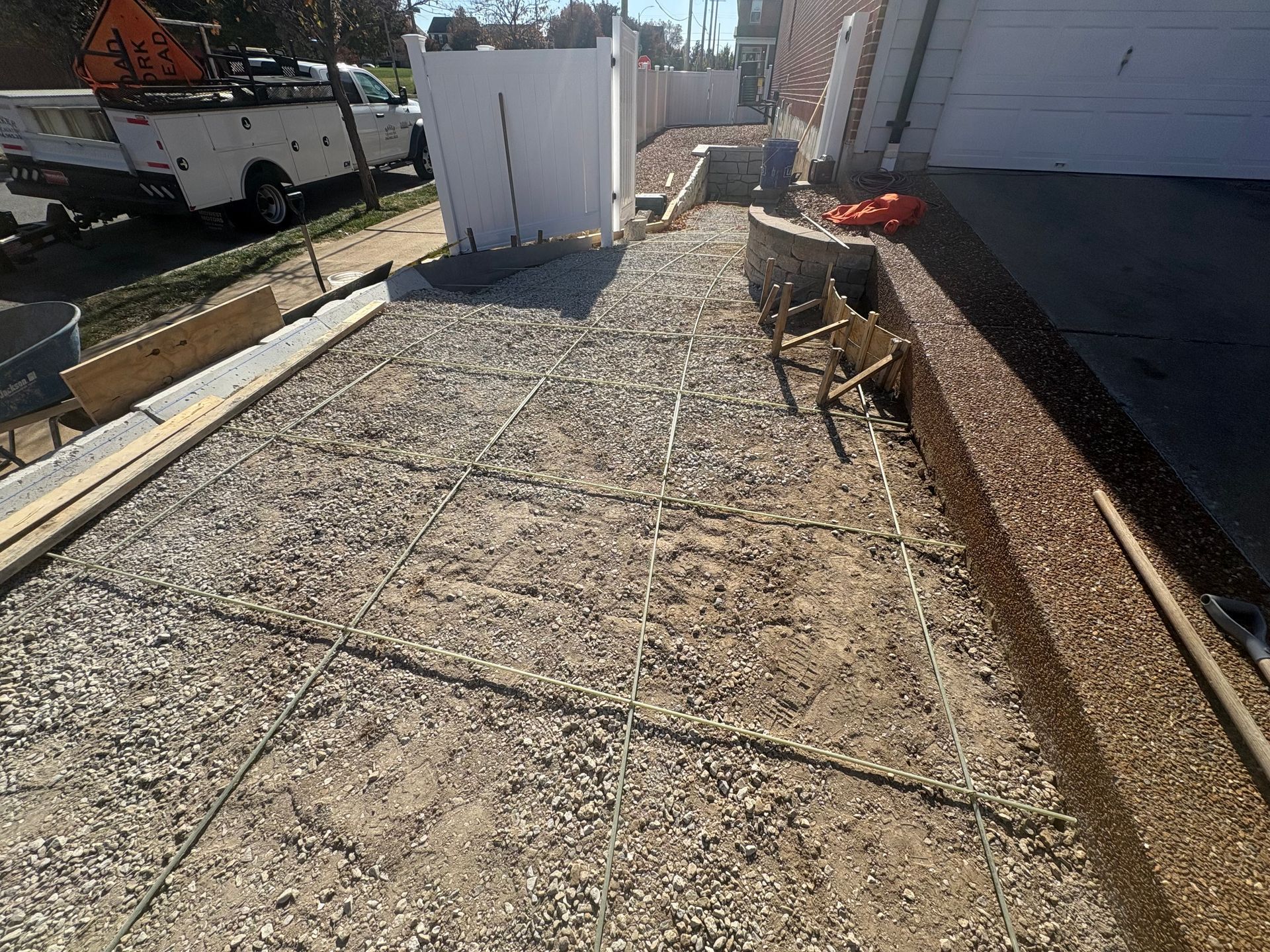Gravel work area beside a house, with wooden edging, utility boxes, and a parked truck in the background.