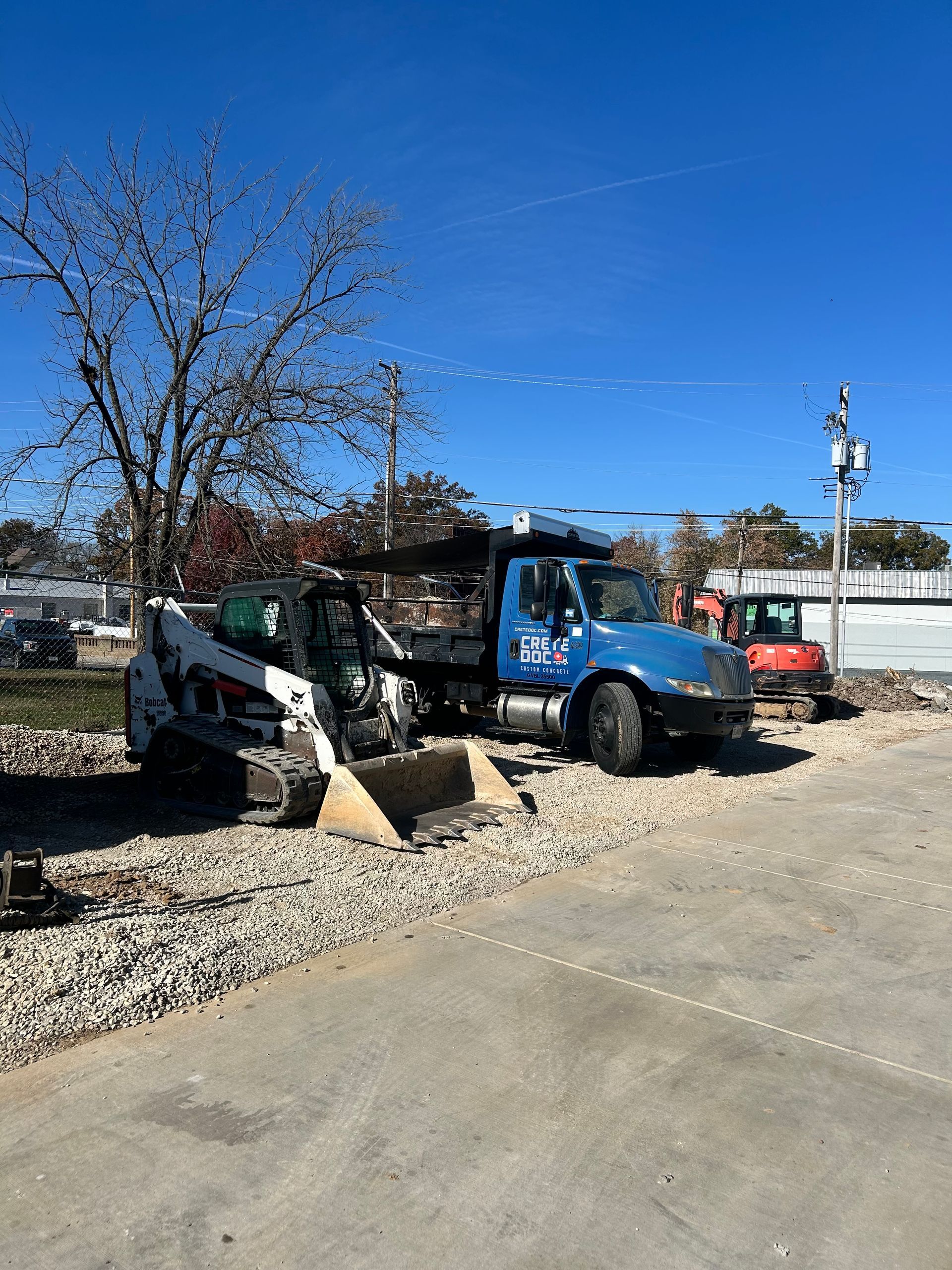 Blue and white dump truck parked beside a gravel pile on a sunny street construction site.