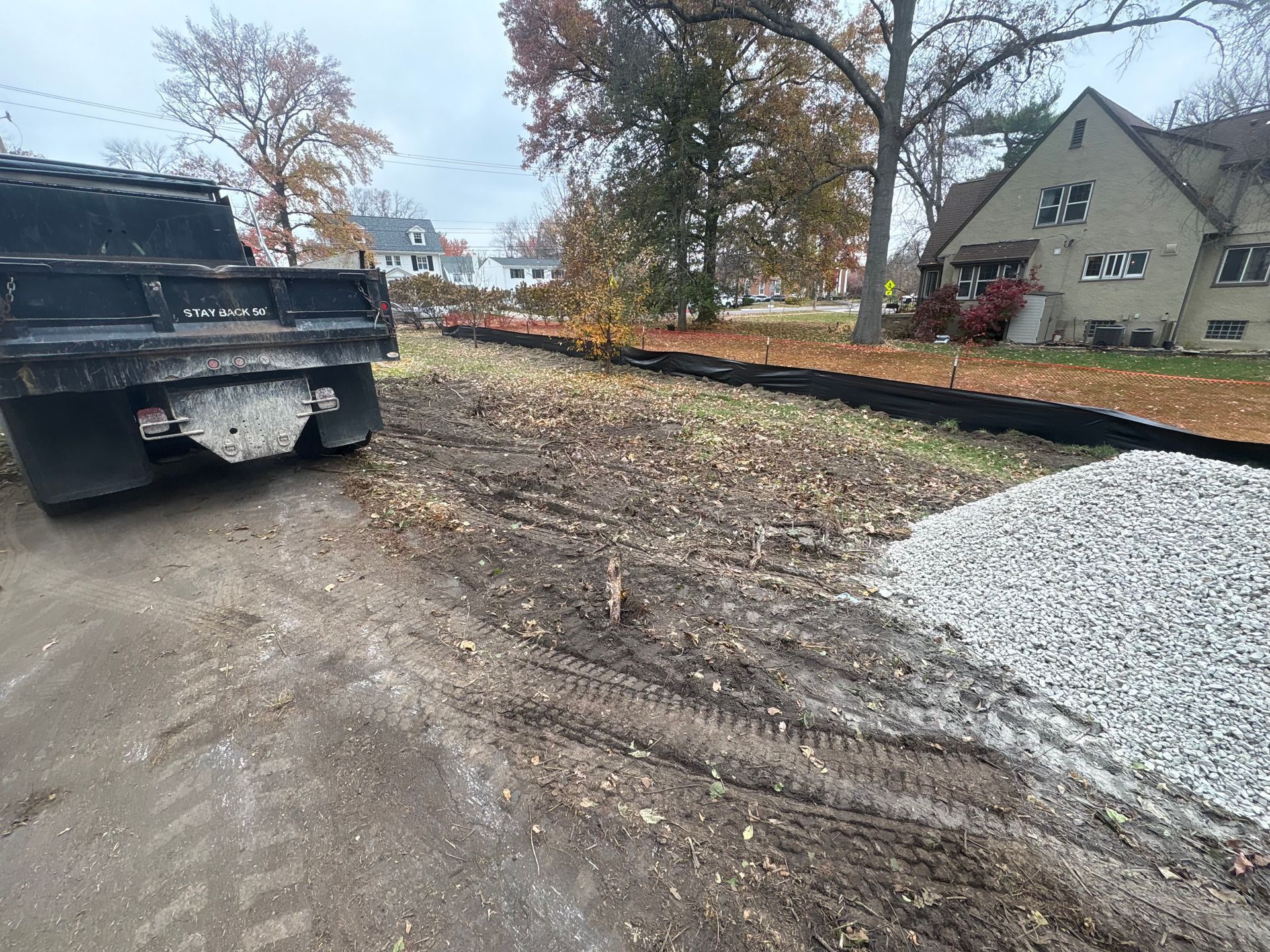 Black pickup parked beside a muddy, leaf-covered path in an autumn neighborhood scene.