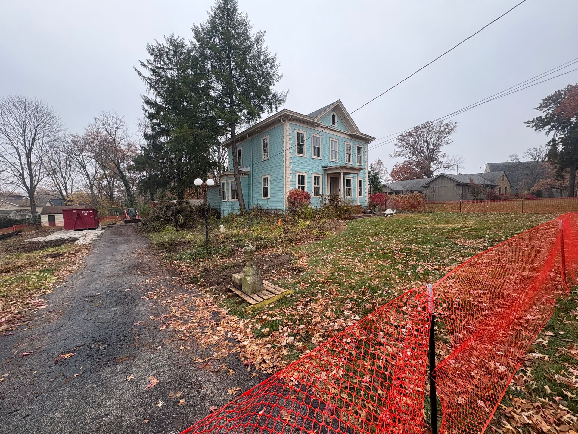 Blue house beside gravel road and orange construction fence on an overcast autumn day.