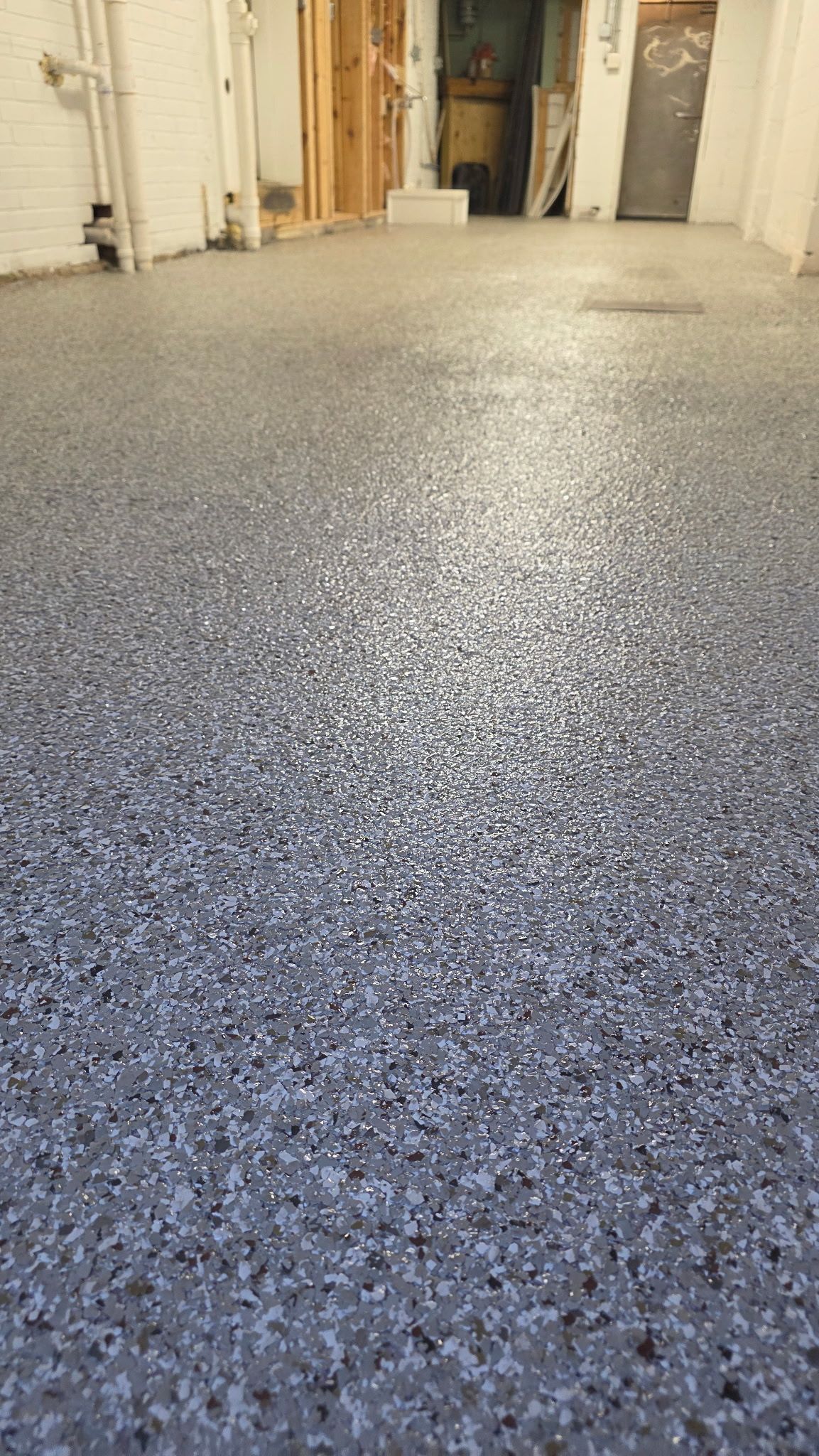 Speckled gray epoxy floor in a garage or storage area, viewed from low angle toward open doors.