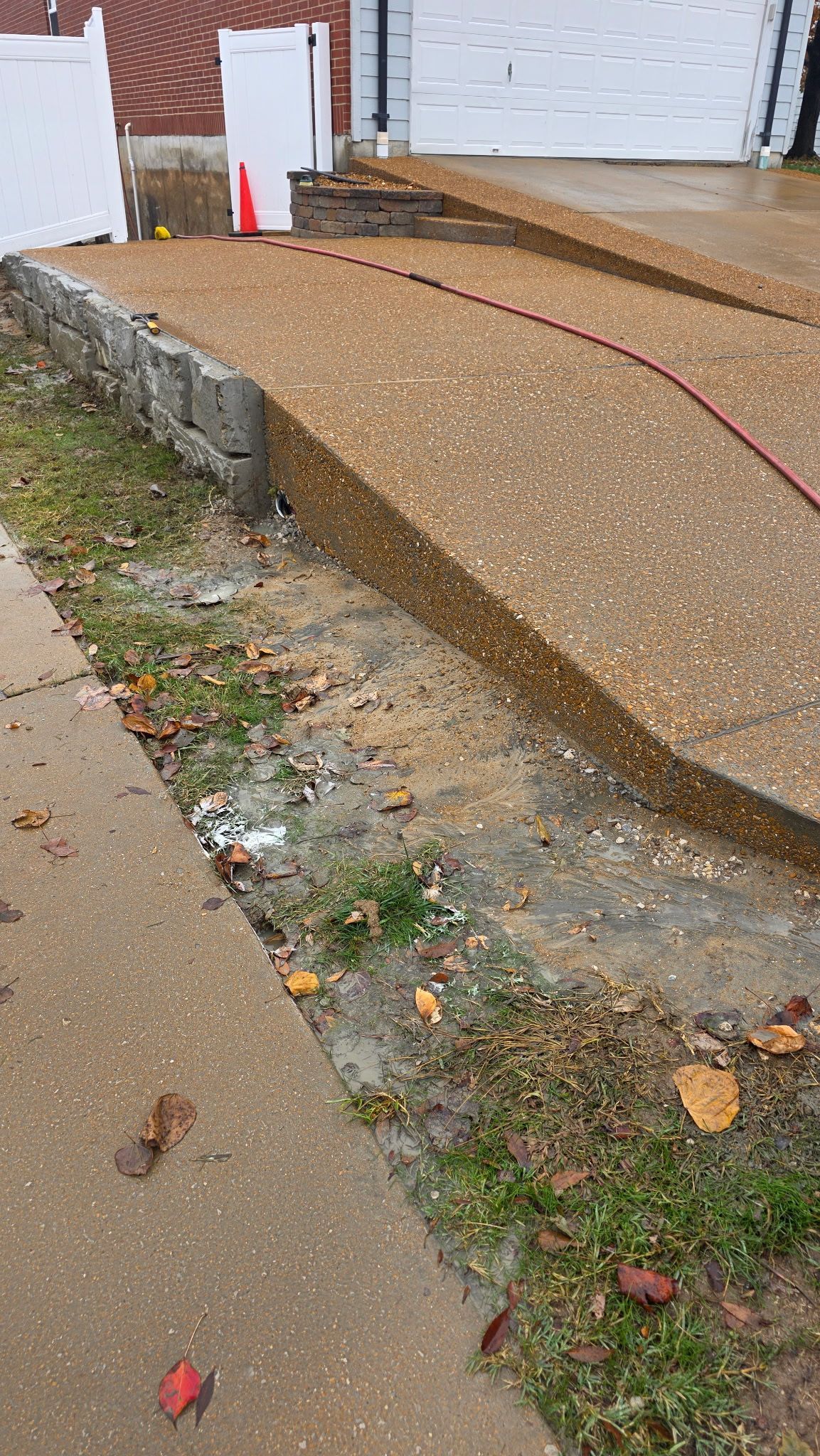 Damaged concrete walkway with a steep eroded slope beside a sidewalk and construction materials nearby.