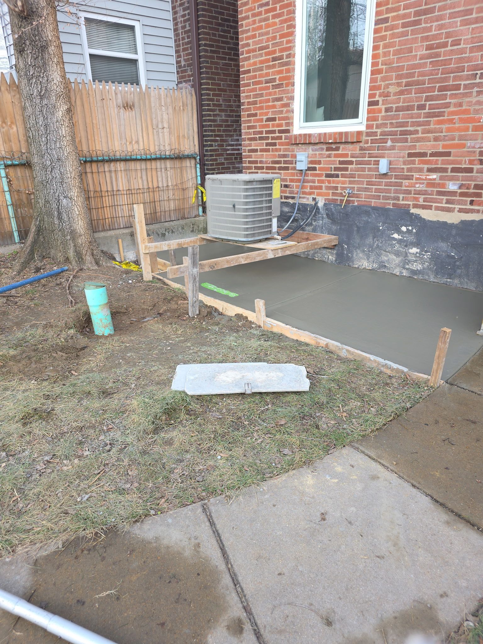 Brick house entrance with a small concrete ramp and wooden handrails beside a wet sidewalk and patchy grass.