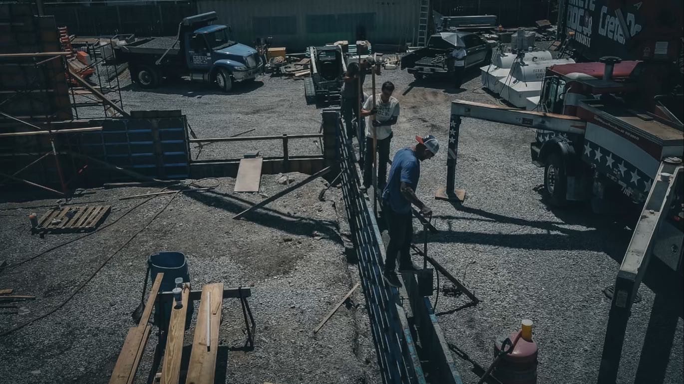 Workers and machinery on a gravel construction site with a large central metal structure.