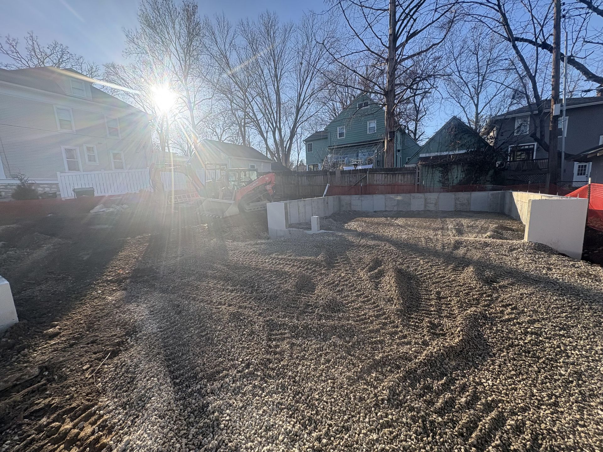 Sunny backyard with bare trees, gravel ground, and houses in the background.