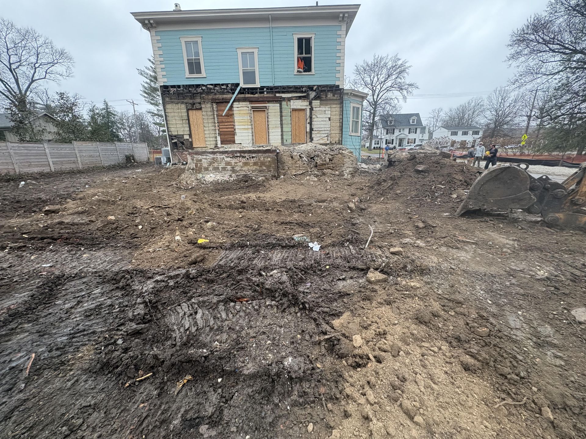 Damp, muddy lot with a weathered two-story house under overcast skies.