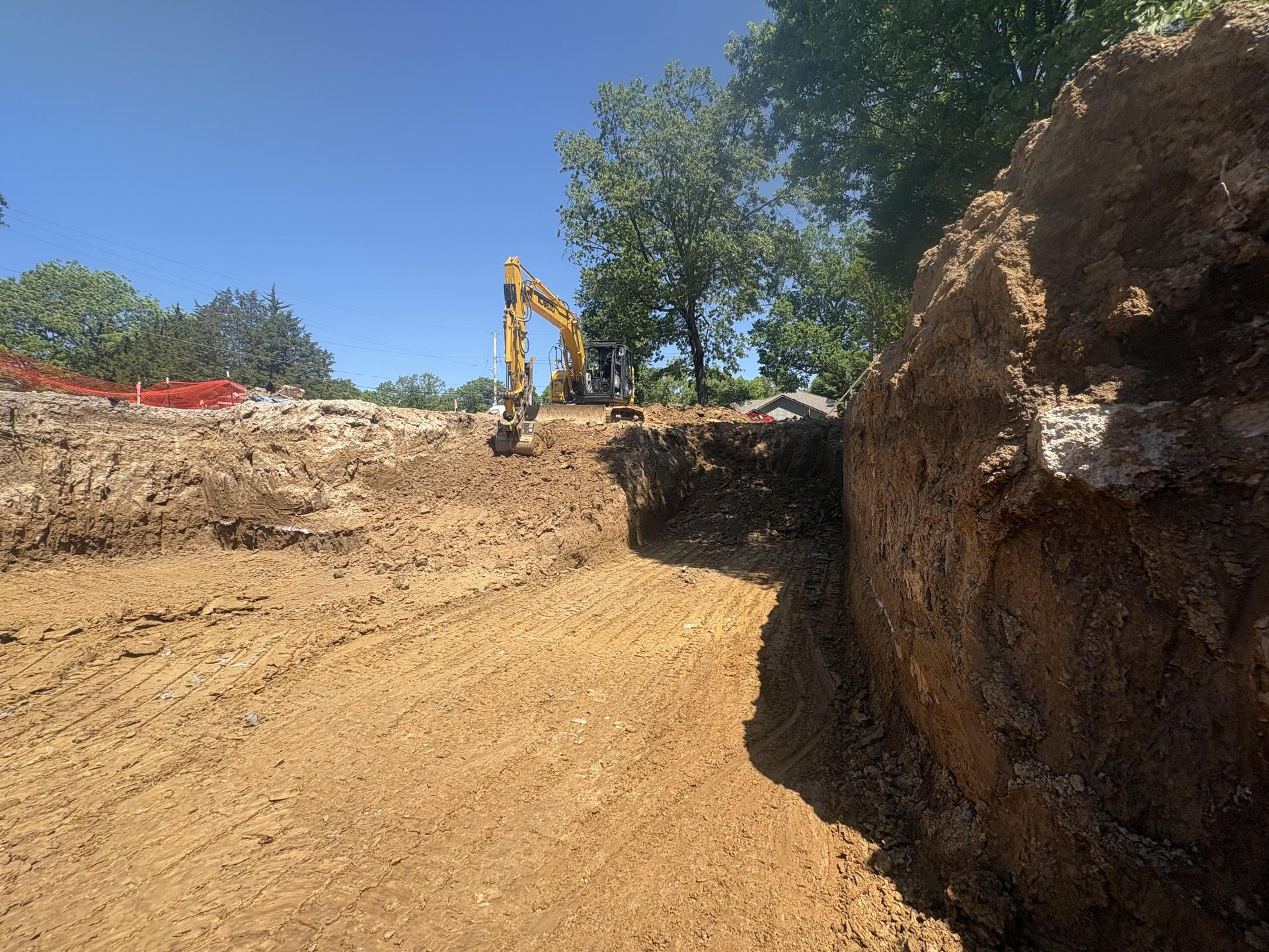 Excavator digging a dirt trench at a construction site under a blue sky.
