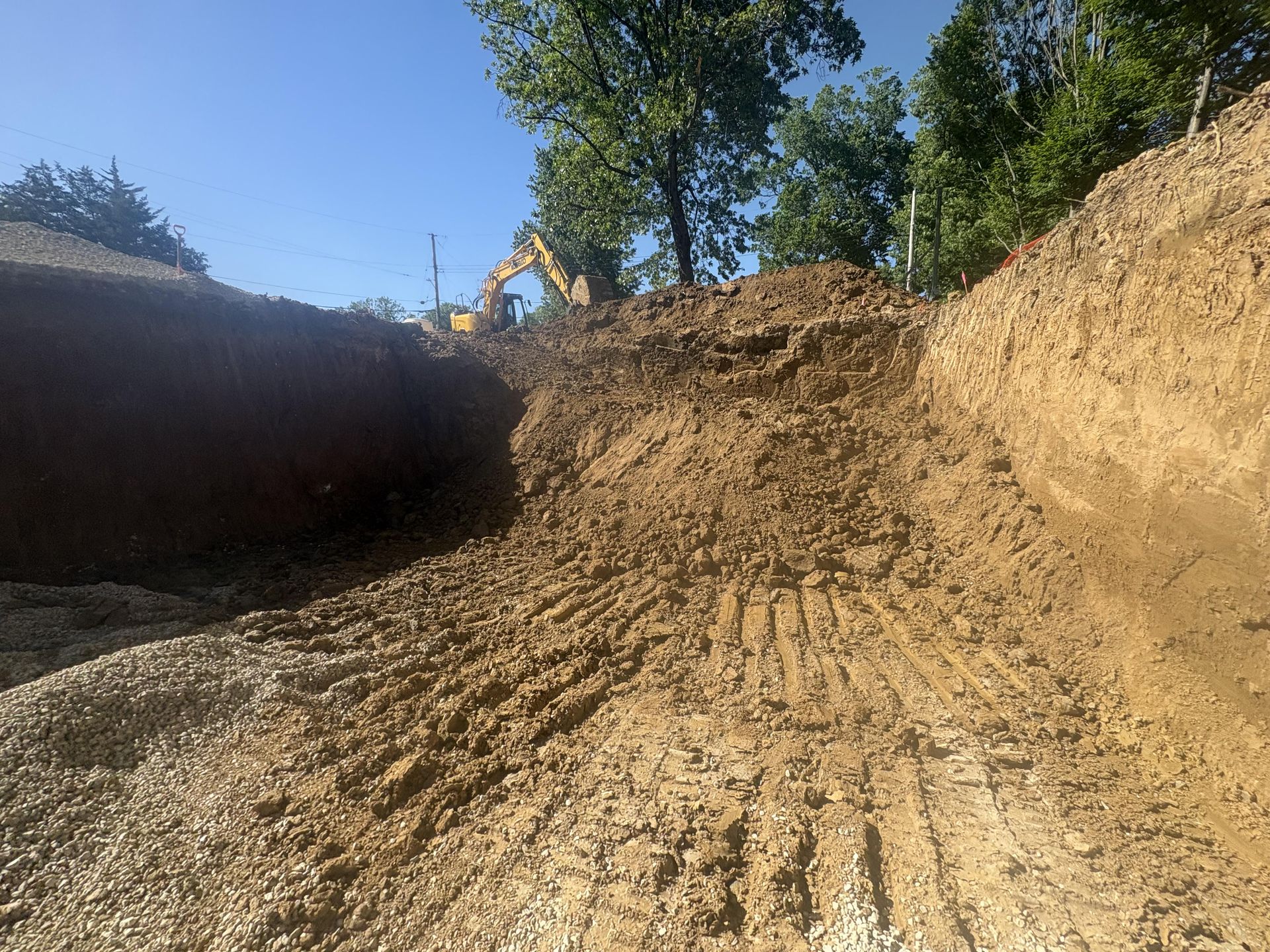 Dirt road cut through earth embankments under a blue sky, with trees along the top edge.