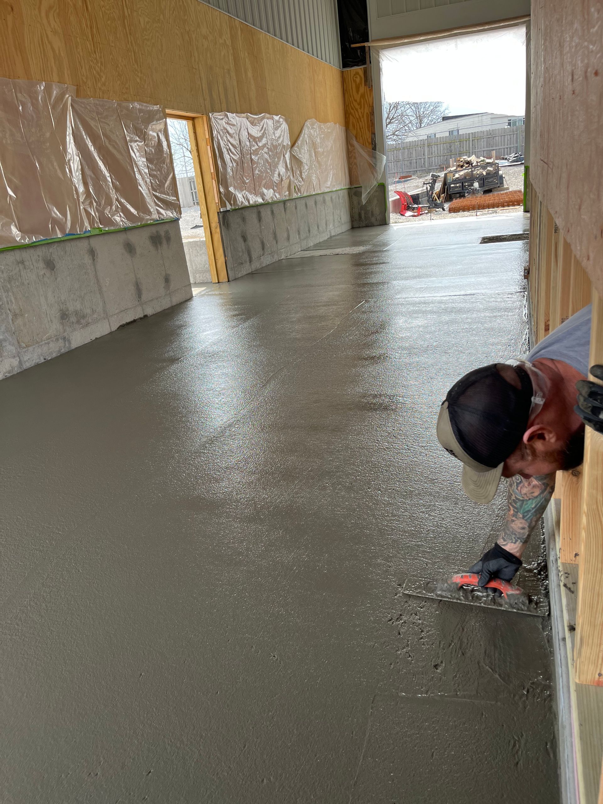 Fresh concrete floor in an unfinished building, with a worker crouched near the right wall.