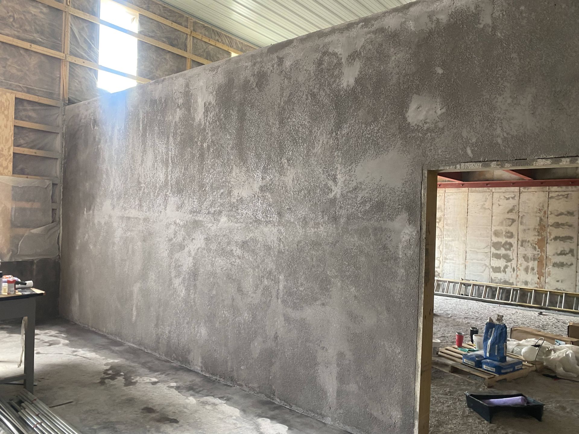 Unfinished concrete wall inside a construction site, with a doorway and tools in the adjoining room.