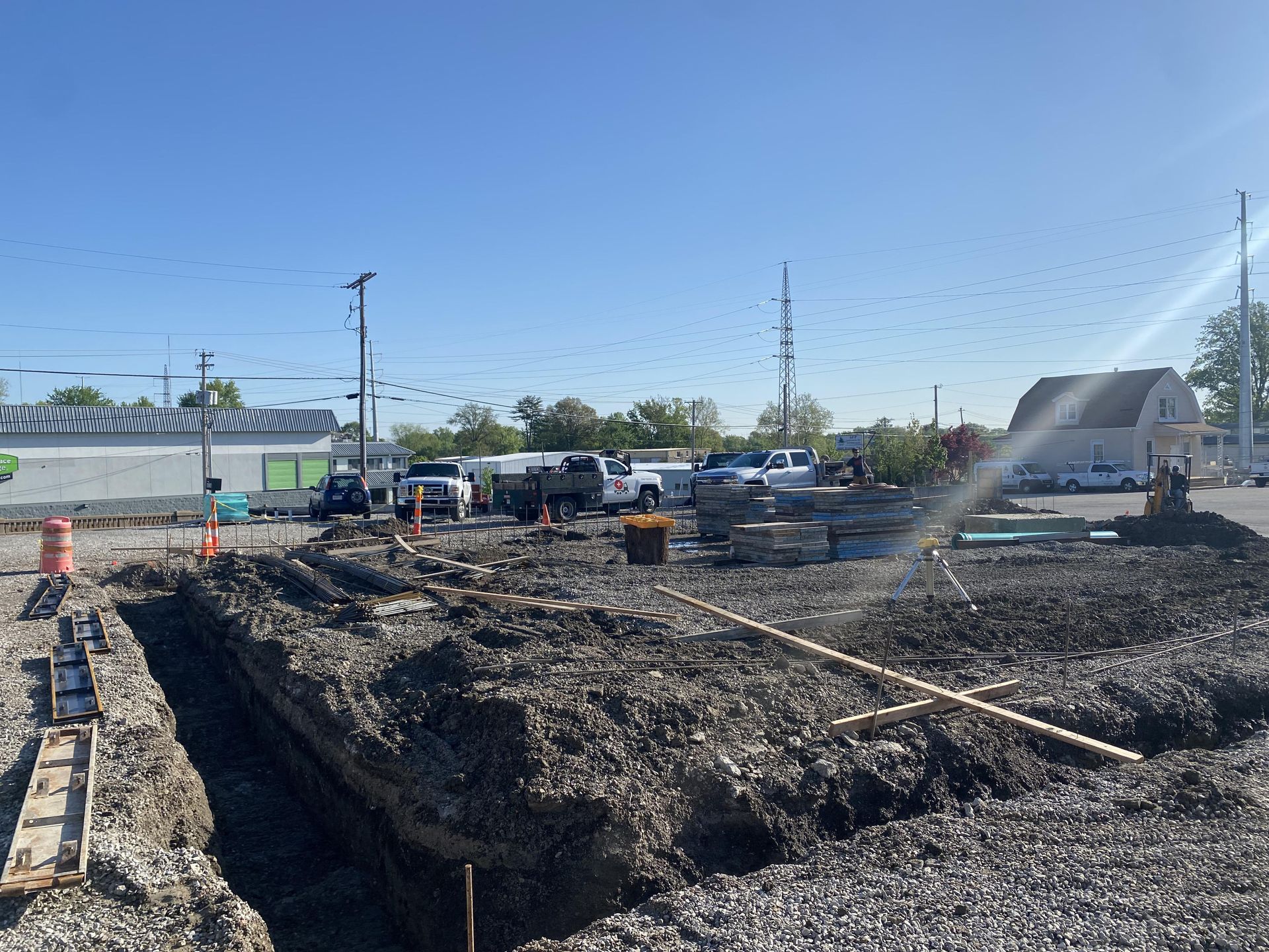 Construction site with a large dirt trench, excavator, trucks, and workers under a clear blue sky.