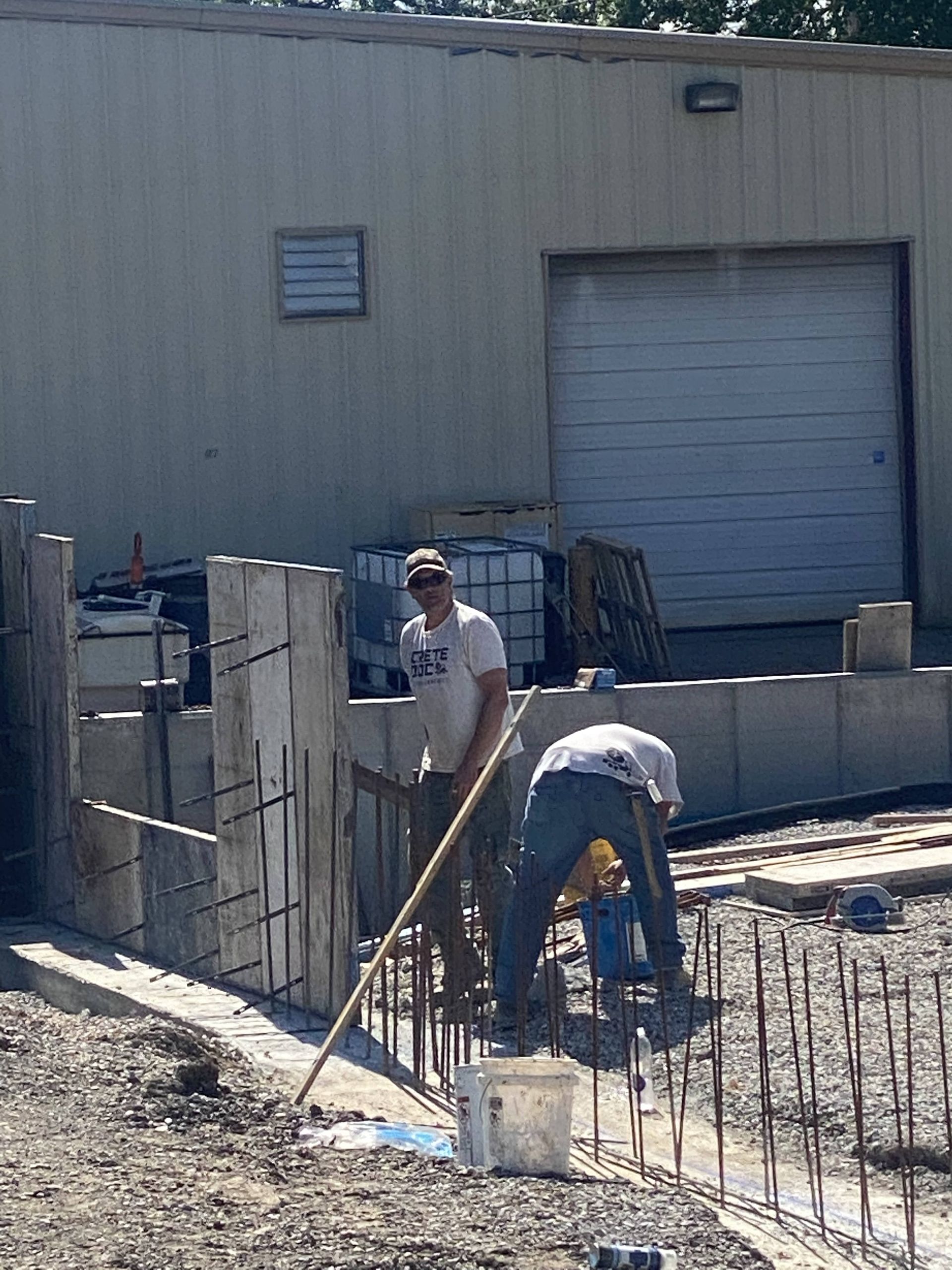 Two workers pour and level concrete beside a warehouse loading dock.