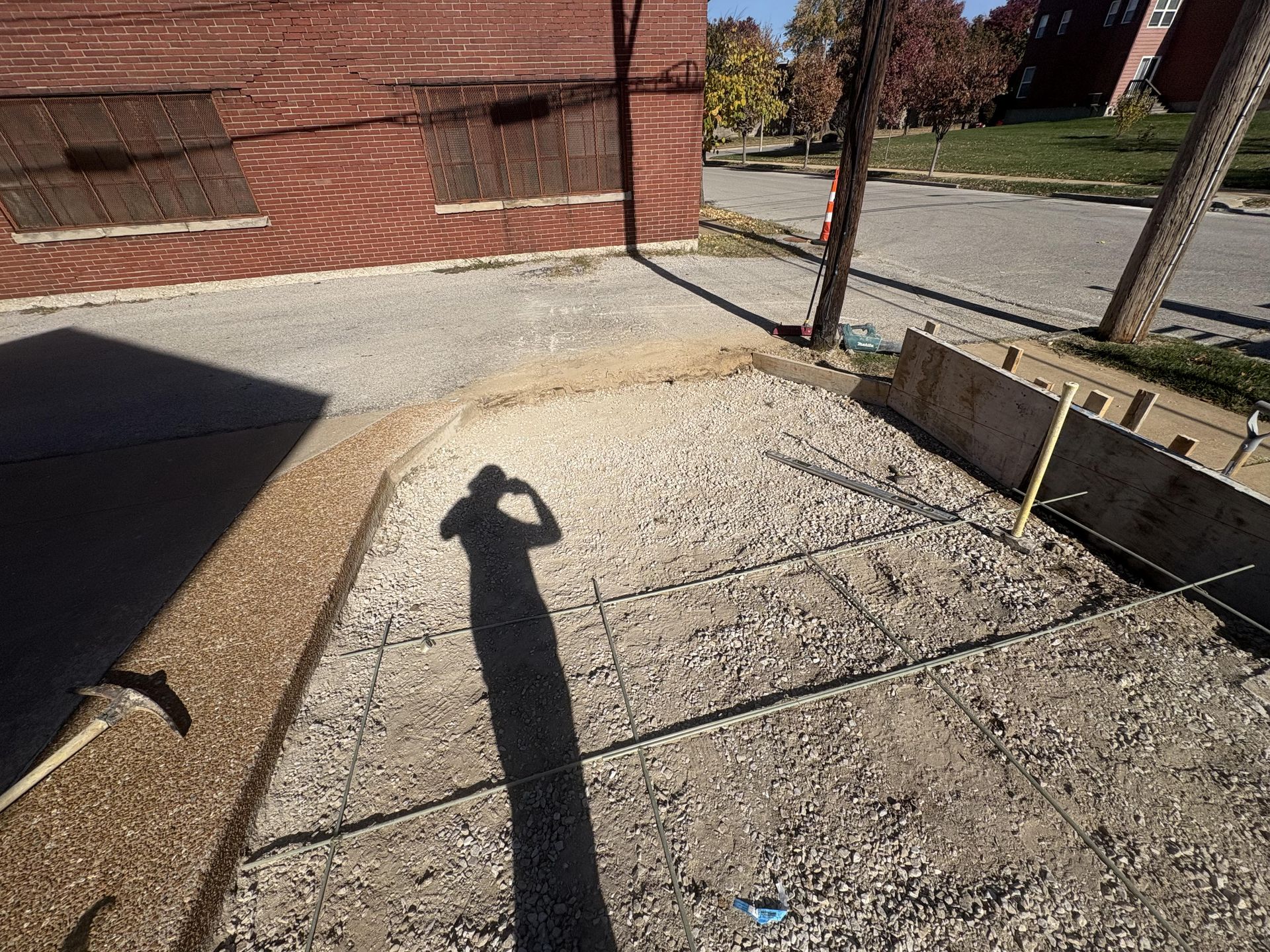 Concrete walkway beside a brick building, with a shadow of a person and a roadside curb in sunlight.