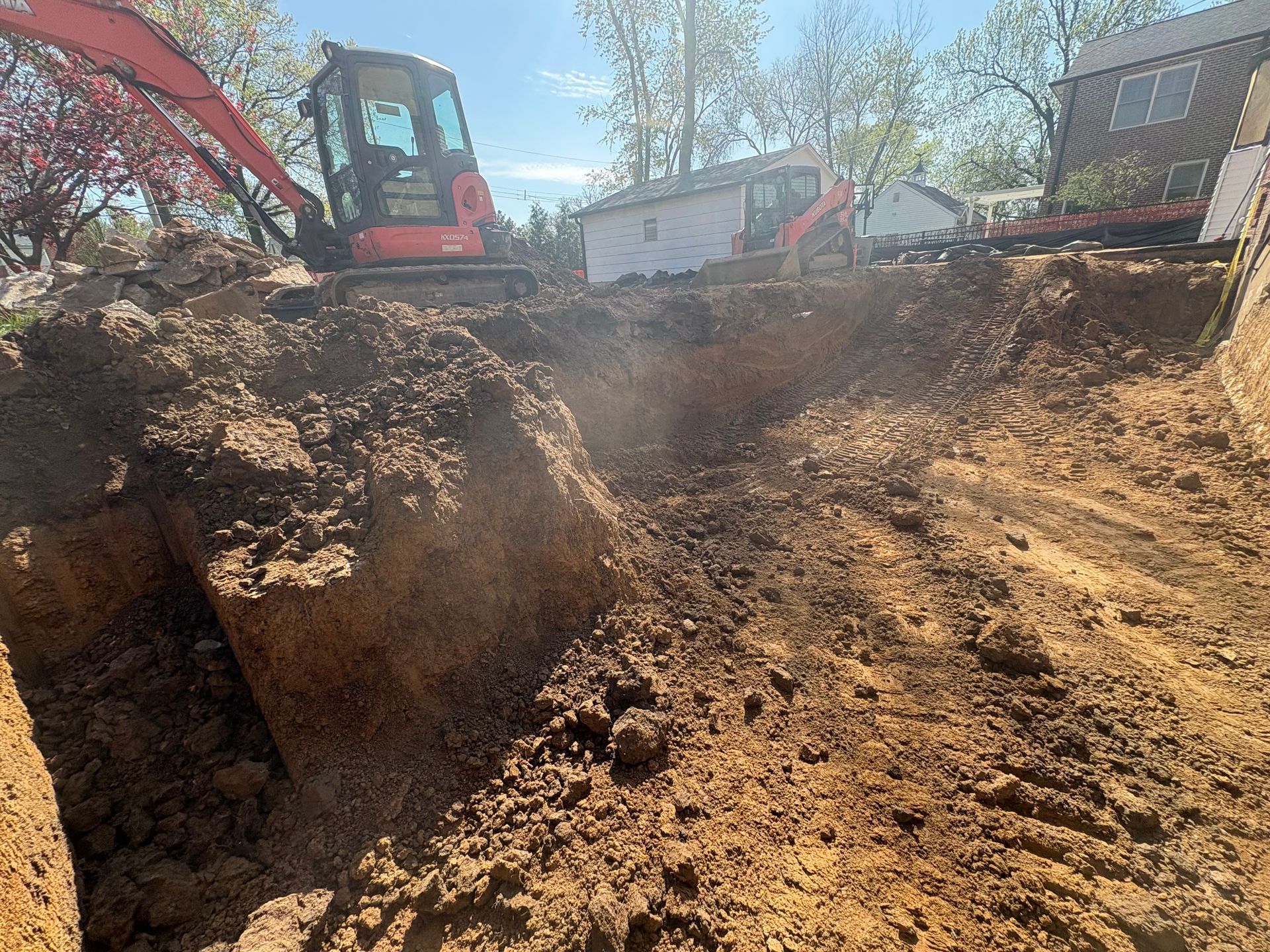 Excavator digging a deep dirt trench at a construction site under a clear sky.