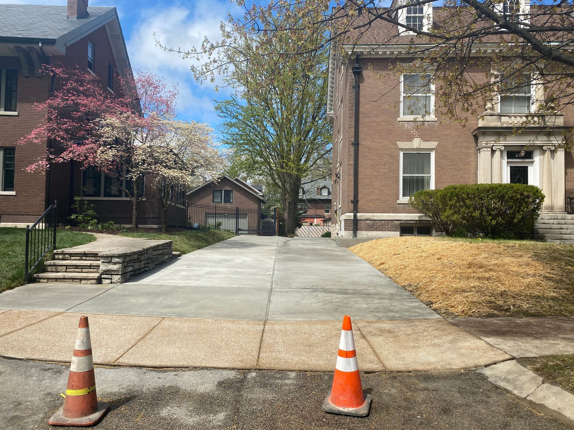 Residential driveway between houses with two orange traffic cones in the foreground.