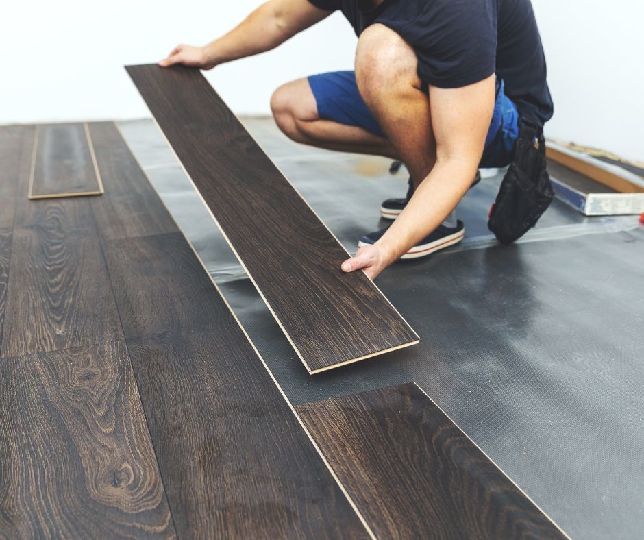 Person installing dark wood flooring on a gray floor surface.