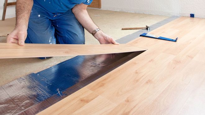 Person lifting a wood plank to reveal a dark floor opening during renovation.