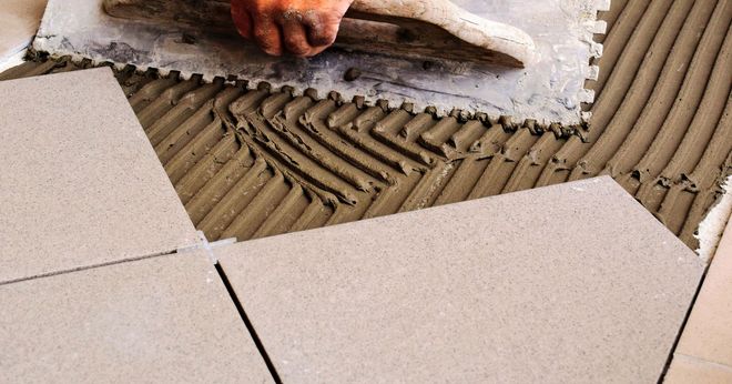 Tile being laid on adhesive mortar, with a hand smoothing the surface.