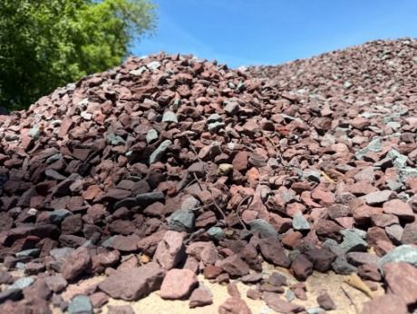 Pile of reddish rocks and gravel outdoors with green trees in the background