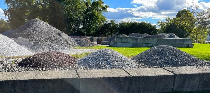 Piles of gray gravel and stone on a concrete ledge in a sunny outdoor yard
