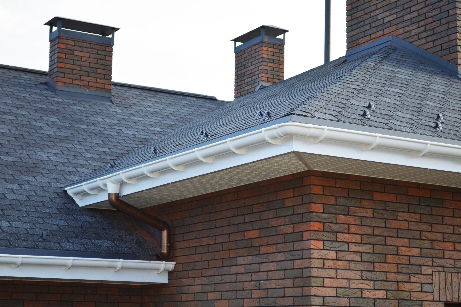 Brick house roof with dark shingles, white trim, and two red-brick chimneys