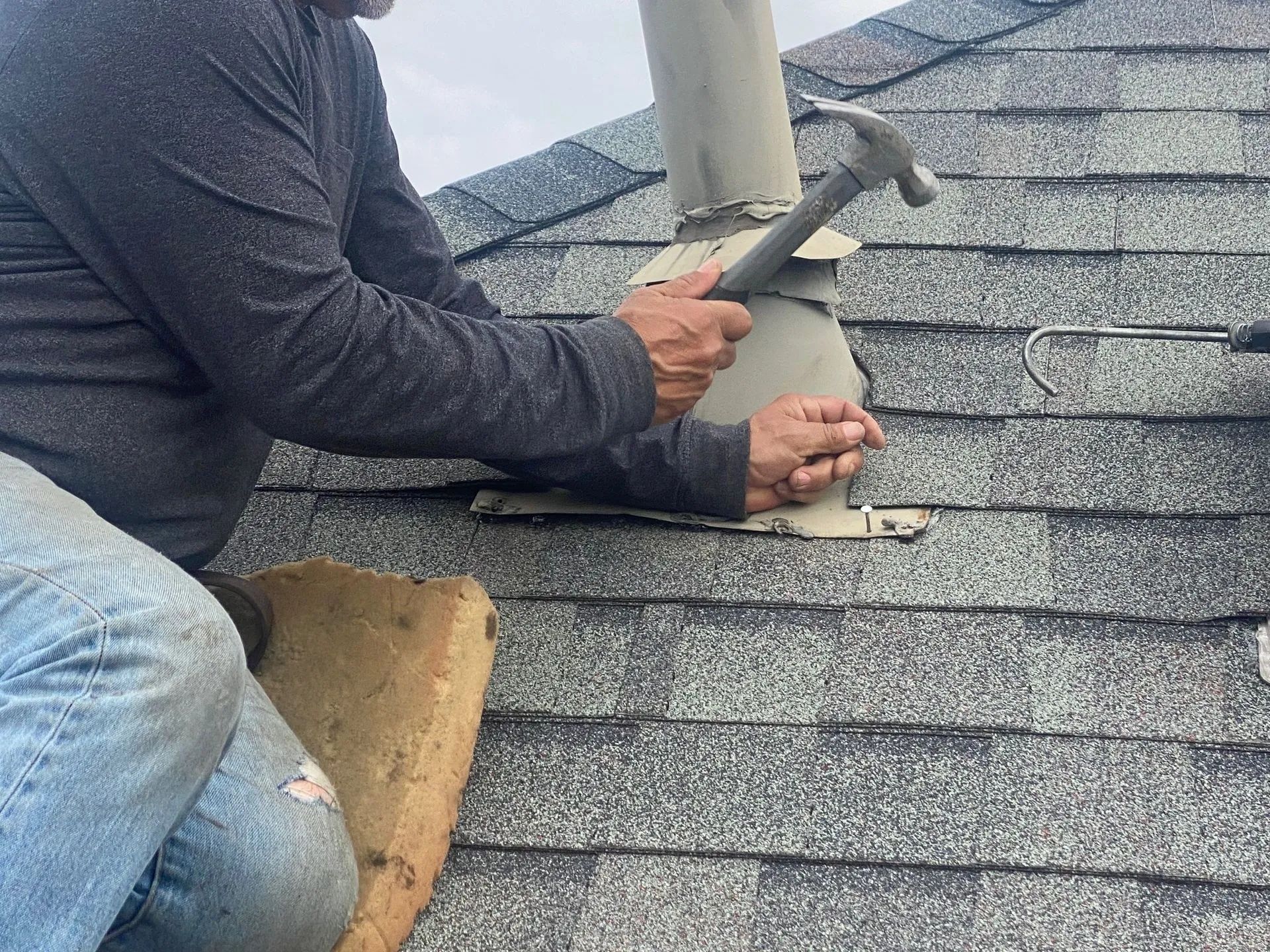 Worker hammering flashing around a roof vent on gray shingle roof