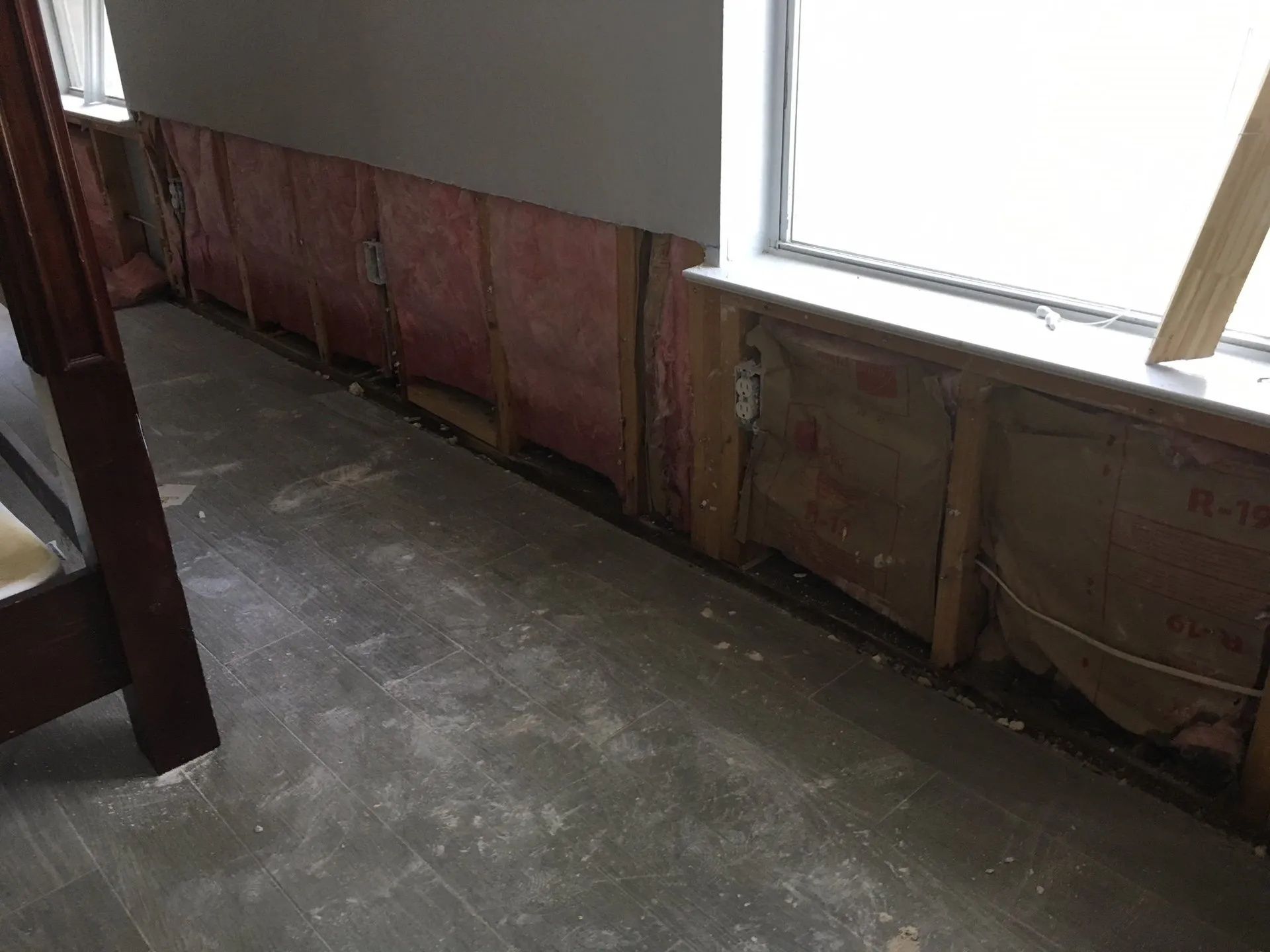 Partially demolished room with exposed wall framing, a window, and a concrete floor covered in dust