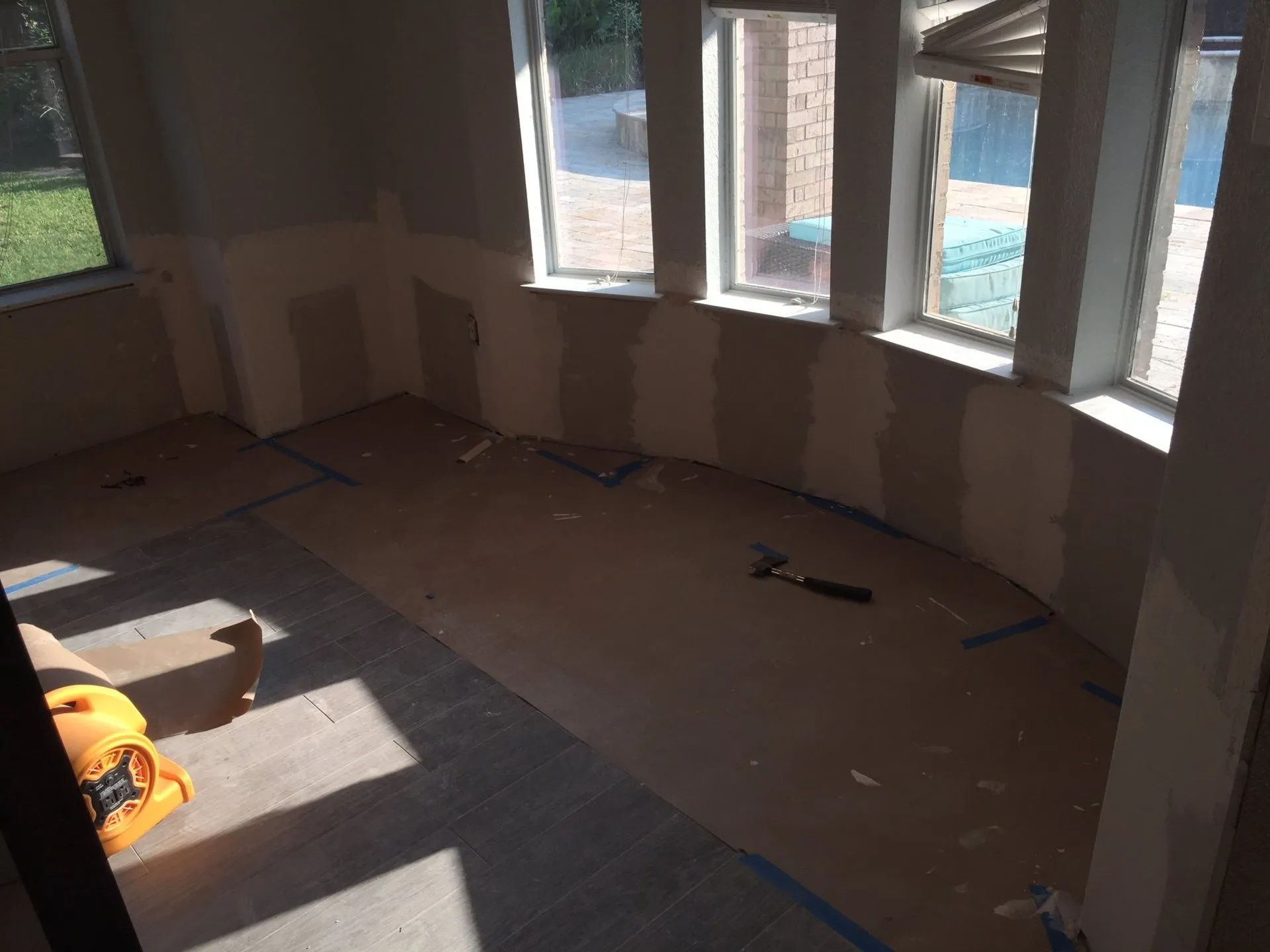 Empty room under renovation with unfinished walls, scattered tools, and sunlight from windows.