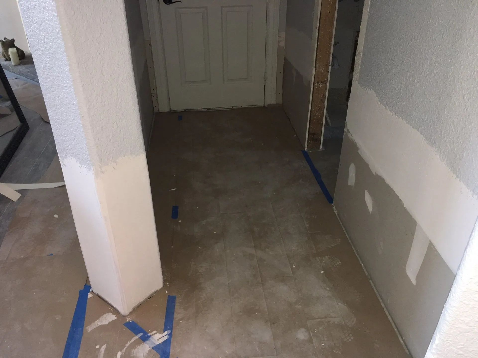 Narrow hallway with unfinished drywall, taped floor edges, and a closed door at the end.