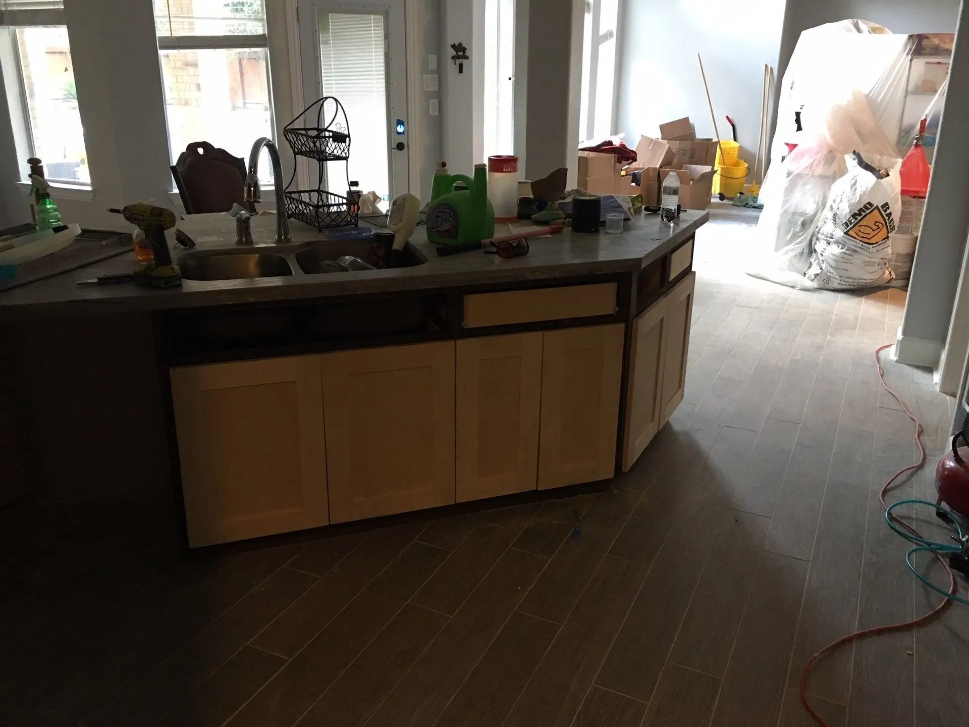 Kitchen with island countertop, sink, cabinets, and cluttered floor, lit by daylight
