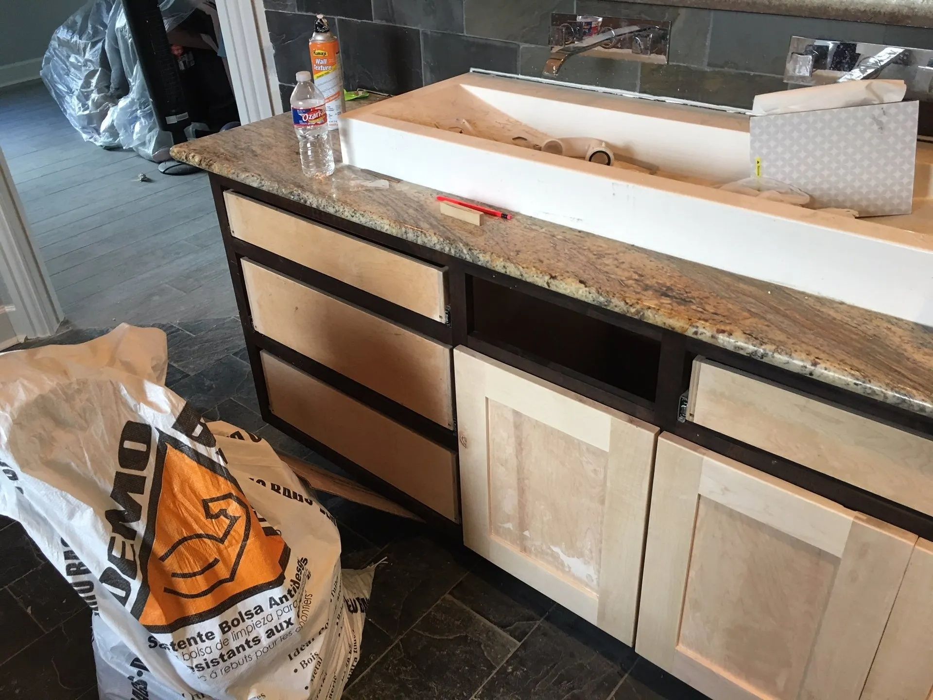 Kitchen counter with granite top, wooden cabinets, and a bag of trash on the floor.