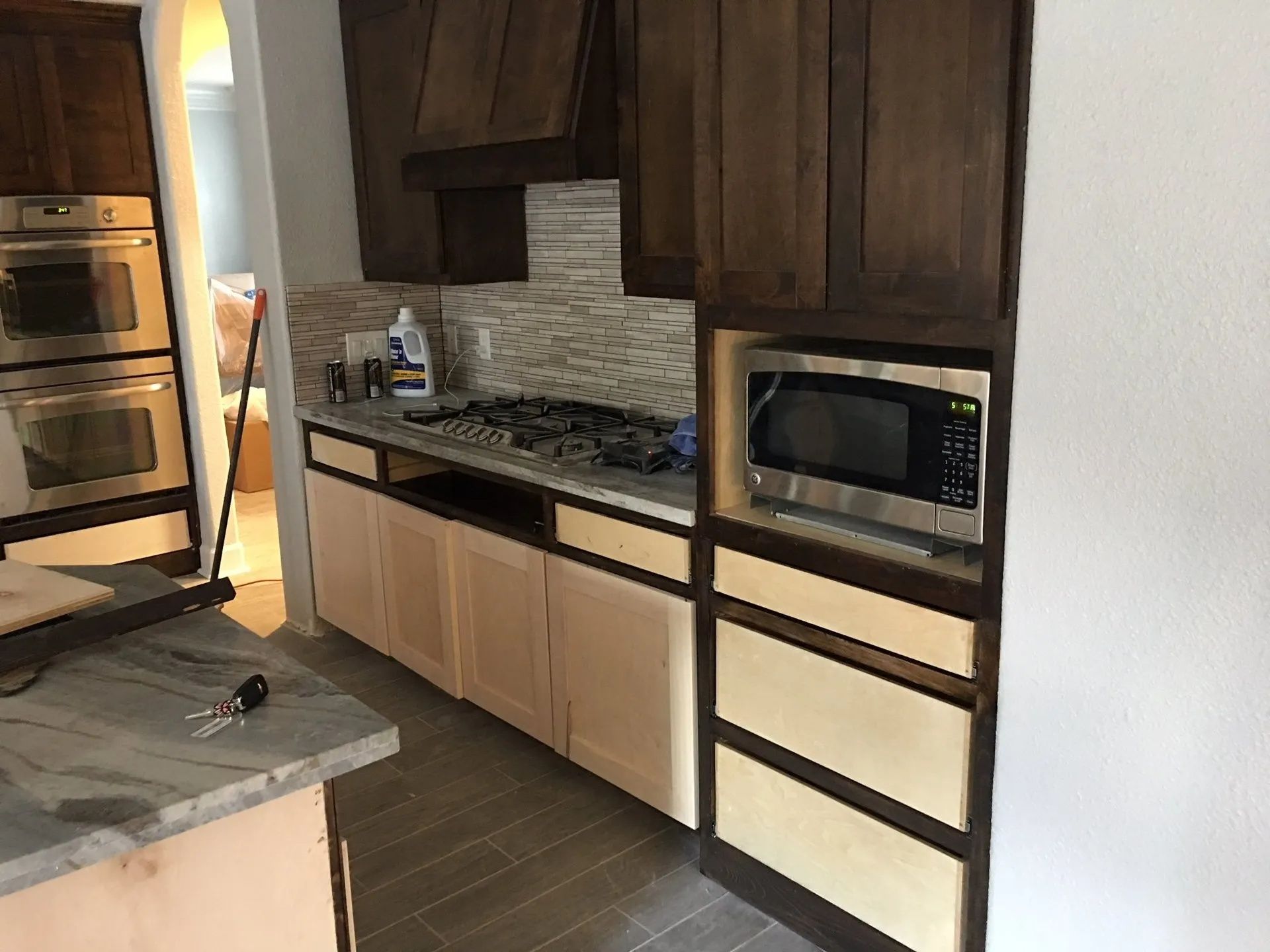 Modern kitchen with dark wood cabinets, light counters, mosaic backsplash, and built-in microwave.