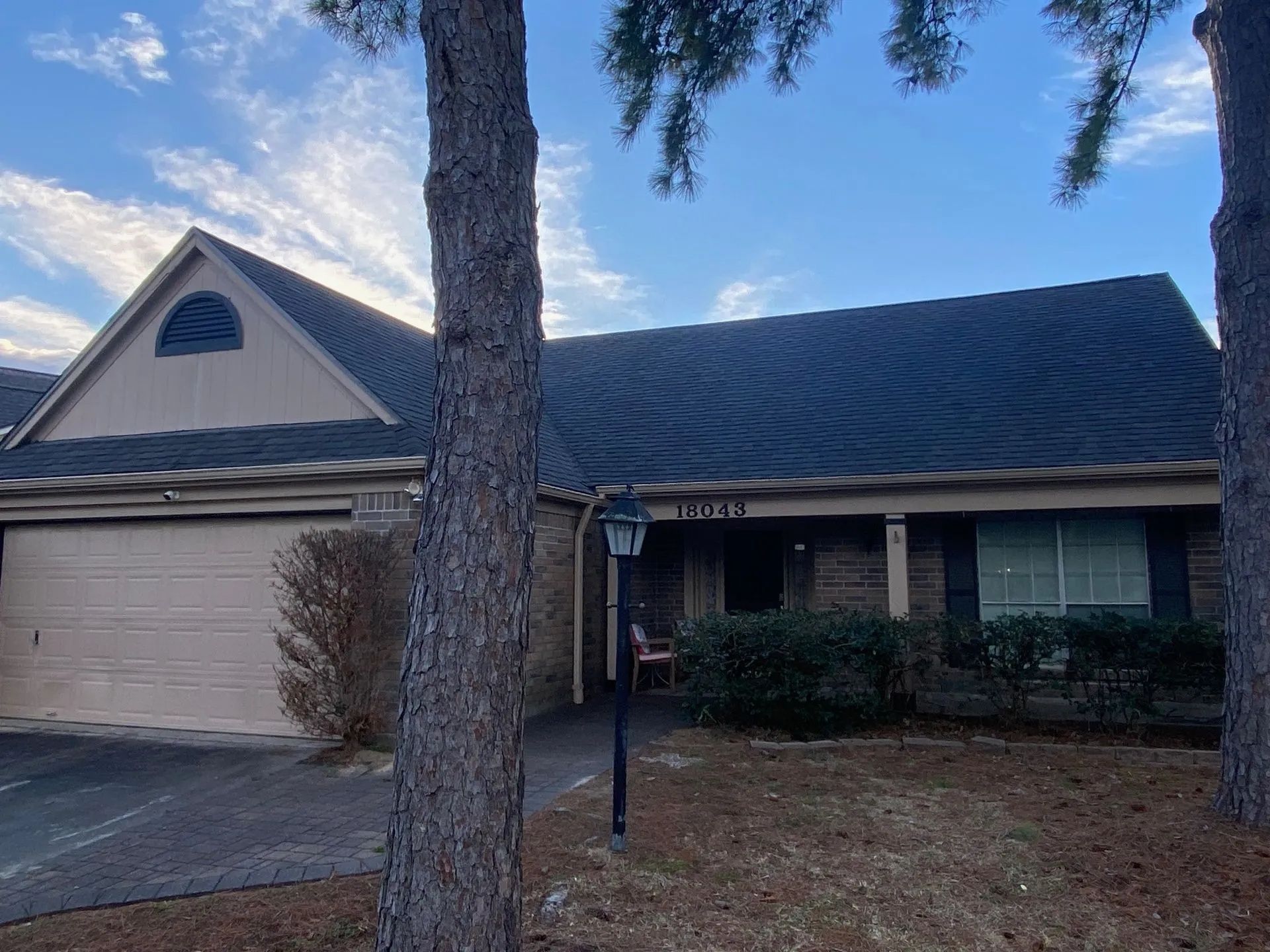 Suburban house with brick facade, garage, and large tree in front yard at dusk