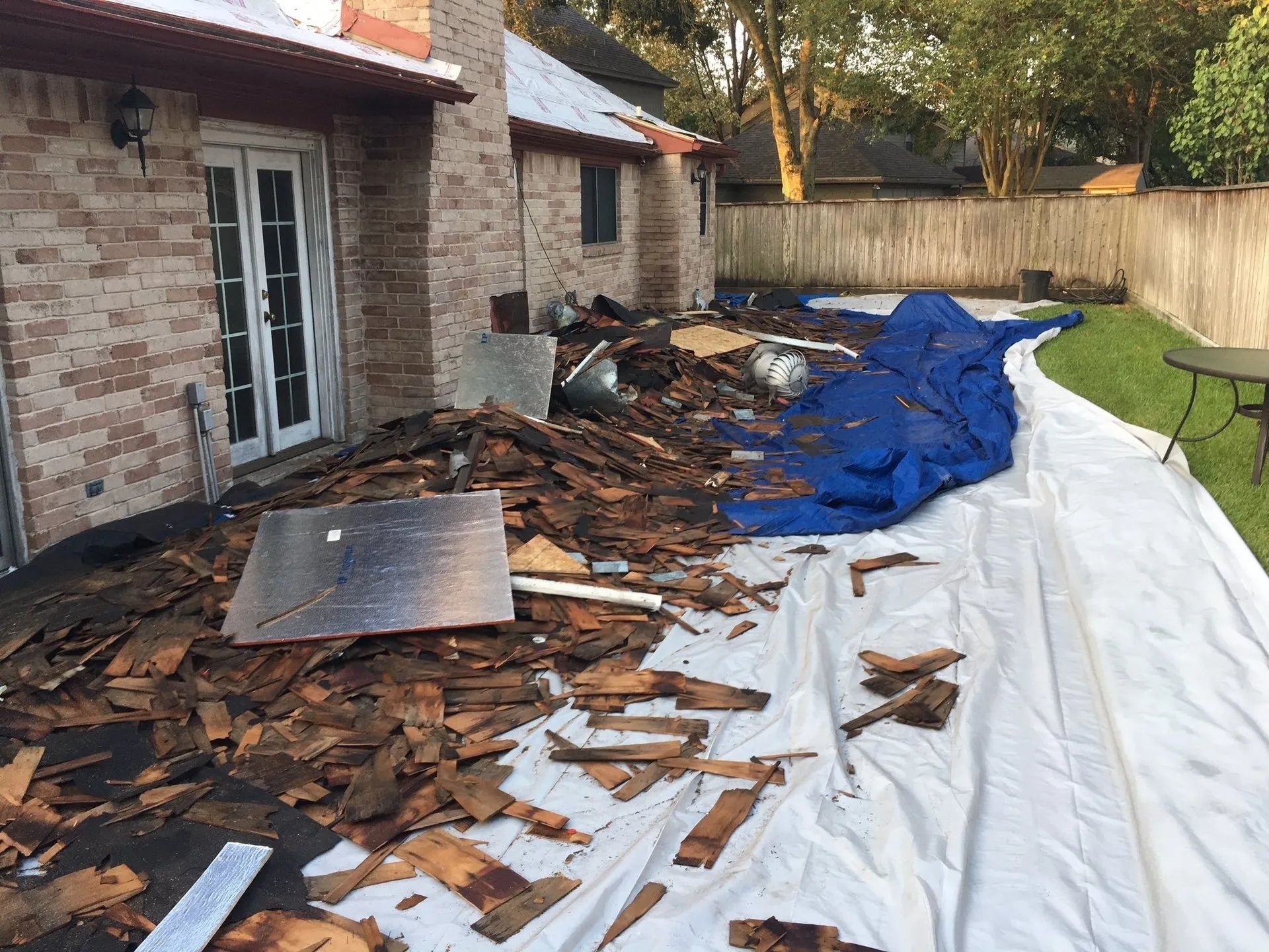 Debris and torn roofing tarp scattered along a house side yard after storm damage