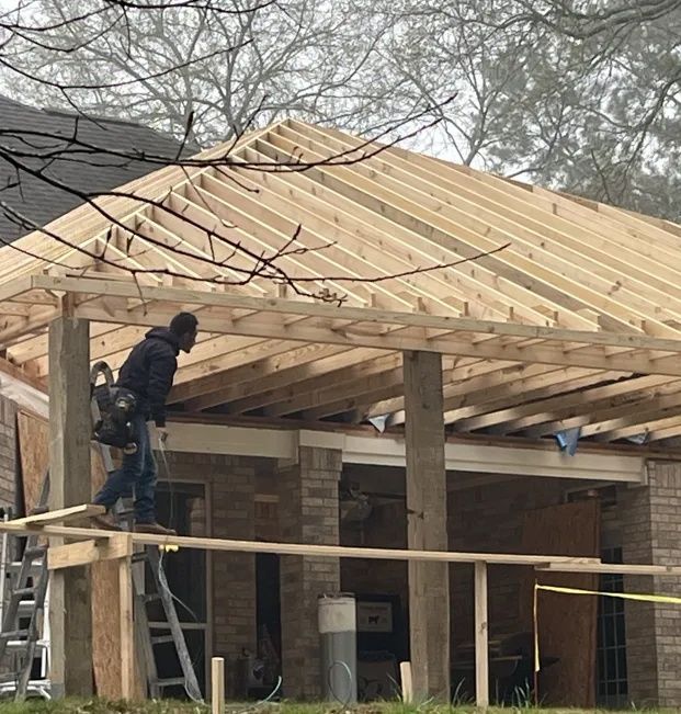Worker on a ladder installing roof framing on a brick building under construction