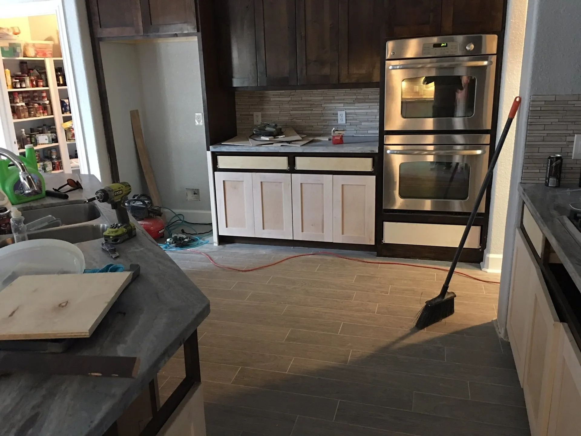 Modern kitchen with dark cabinets, stainless oven, white lower cabinets, and a broom on the floor.