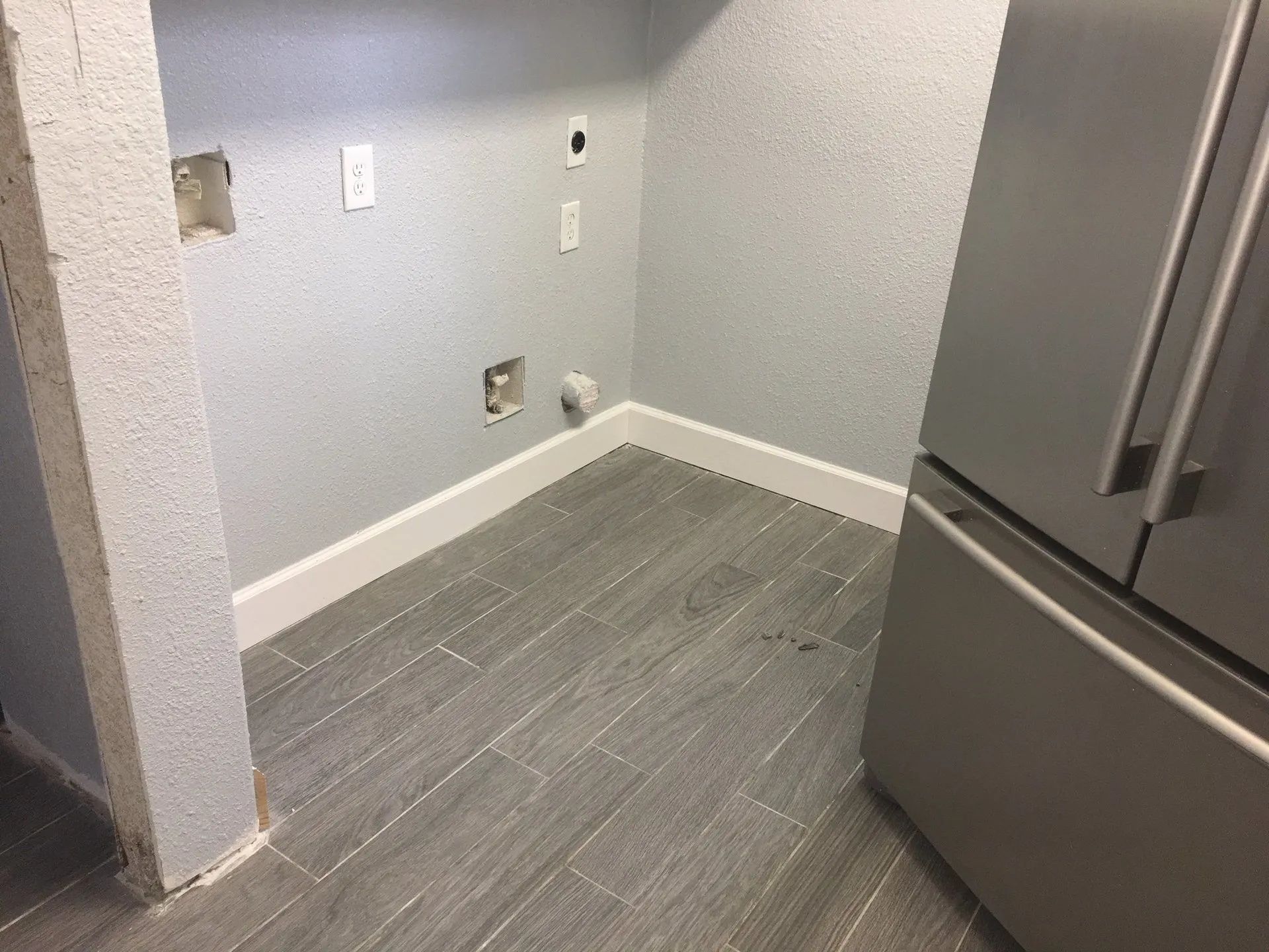 Empty kitchen corner with gray tile floor, light gray walls, and stainless steel refrigerator.