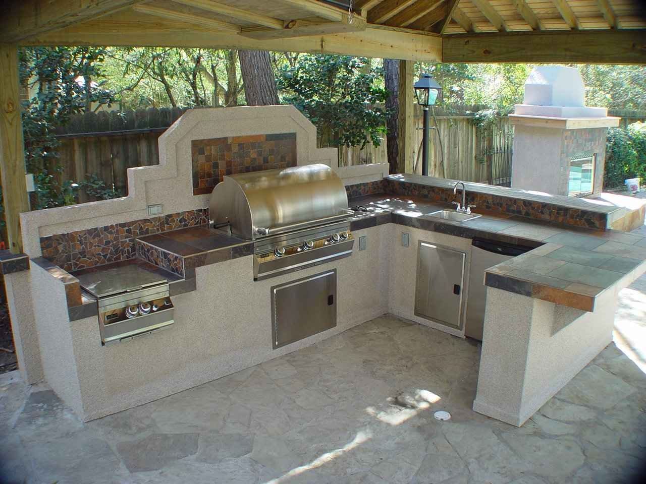 Outdoor stone barbecue kitchen under a wooden gazebo with built-in grill and counter seating