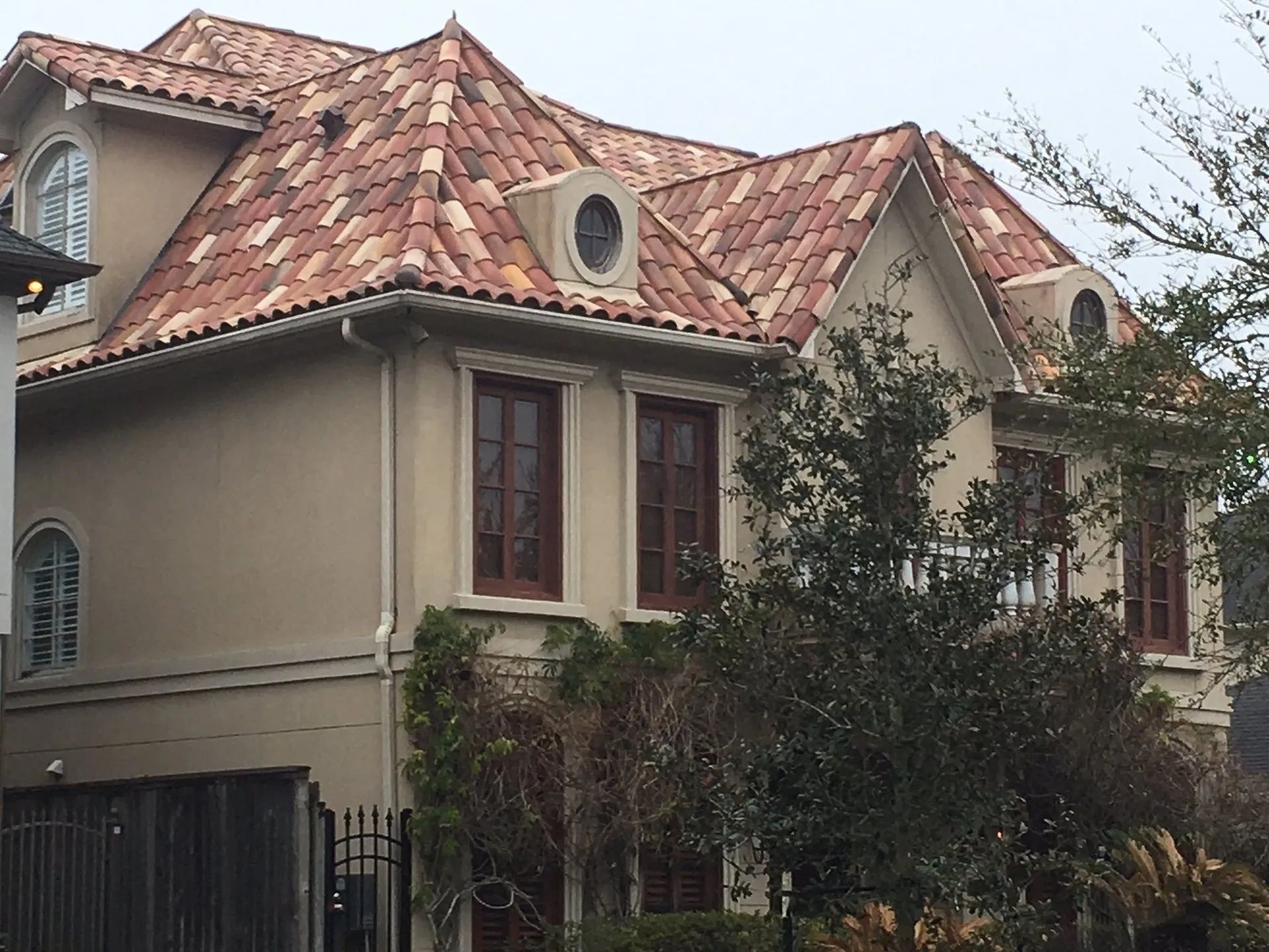 Two-story house with red tile roof, beige walls, and small trees in the front yard