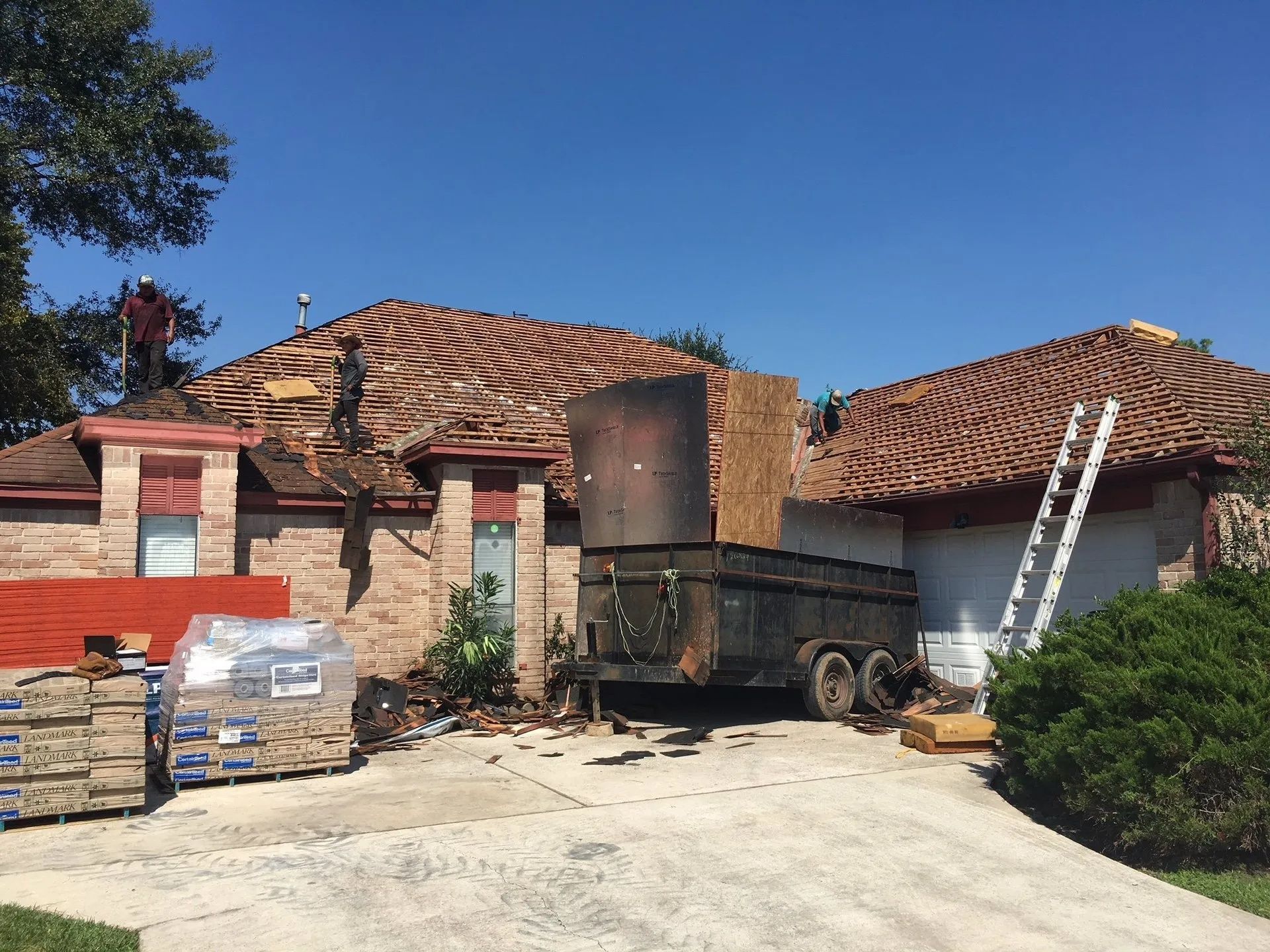 Rural courtyard with tiled-roof houses, a truck, stacked pallets, and a ladder under a blue sky