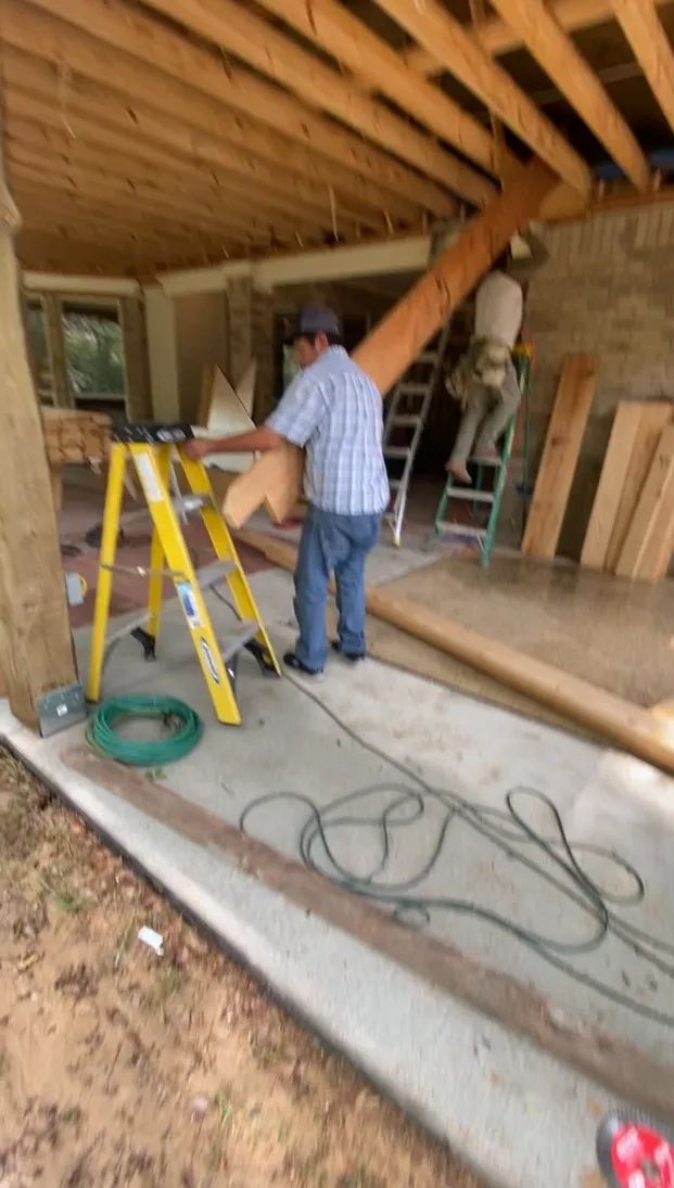 Person working in a partially finished garage with ladders, wooden beams, and tools on the floor
