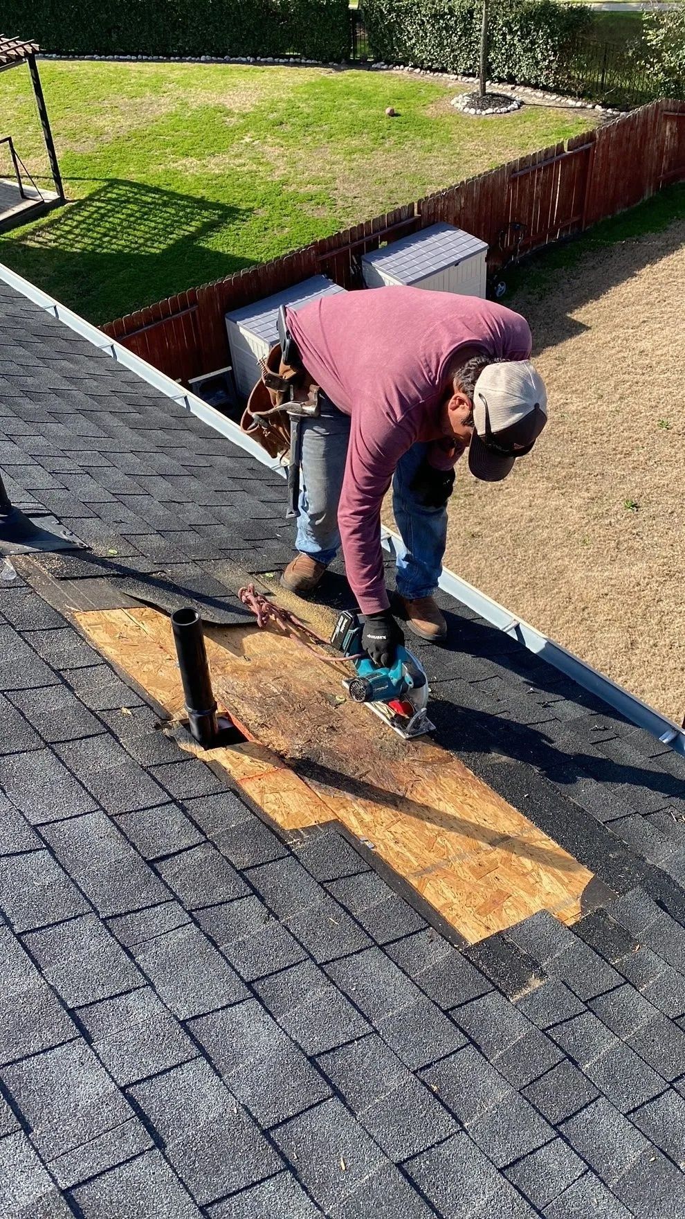 Worker fixing roof shingles with a power tool on a house rooftop.