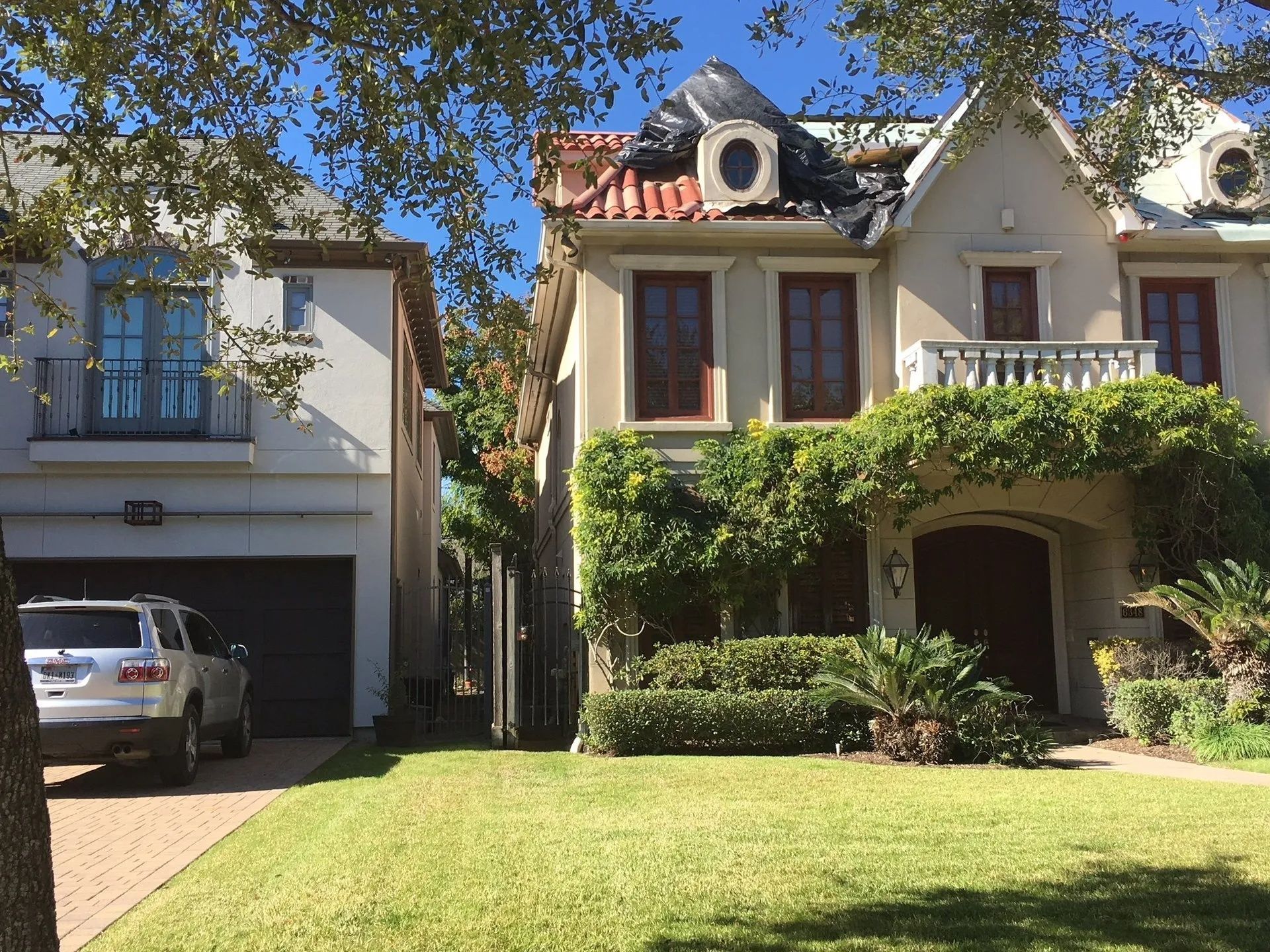A sunny suburban house with a red roof, garage, and ivy-covered front porch beside a parked car.