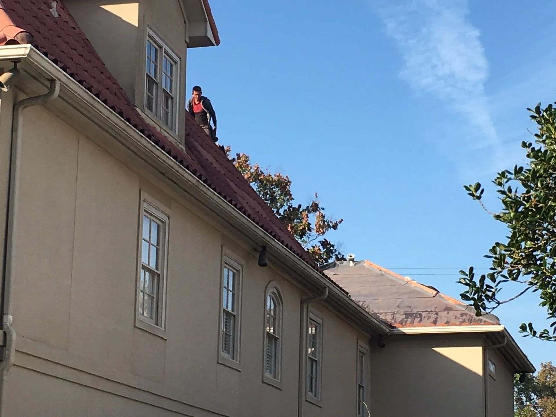 Person in a red jacket on a rooftop beside a beige building under a blue sky.