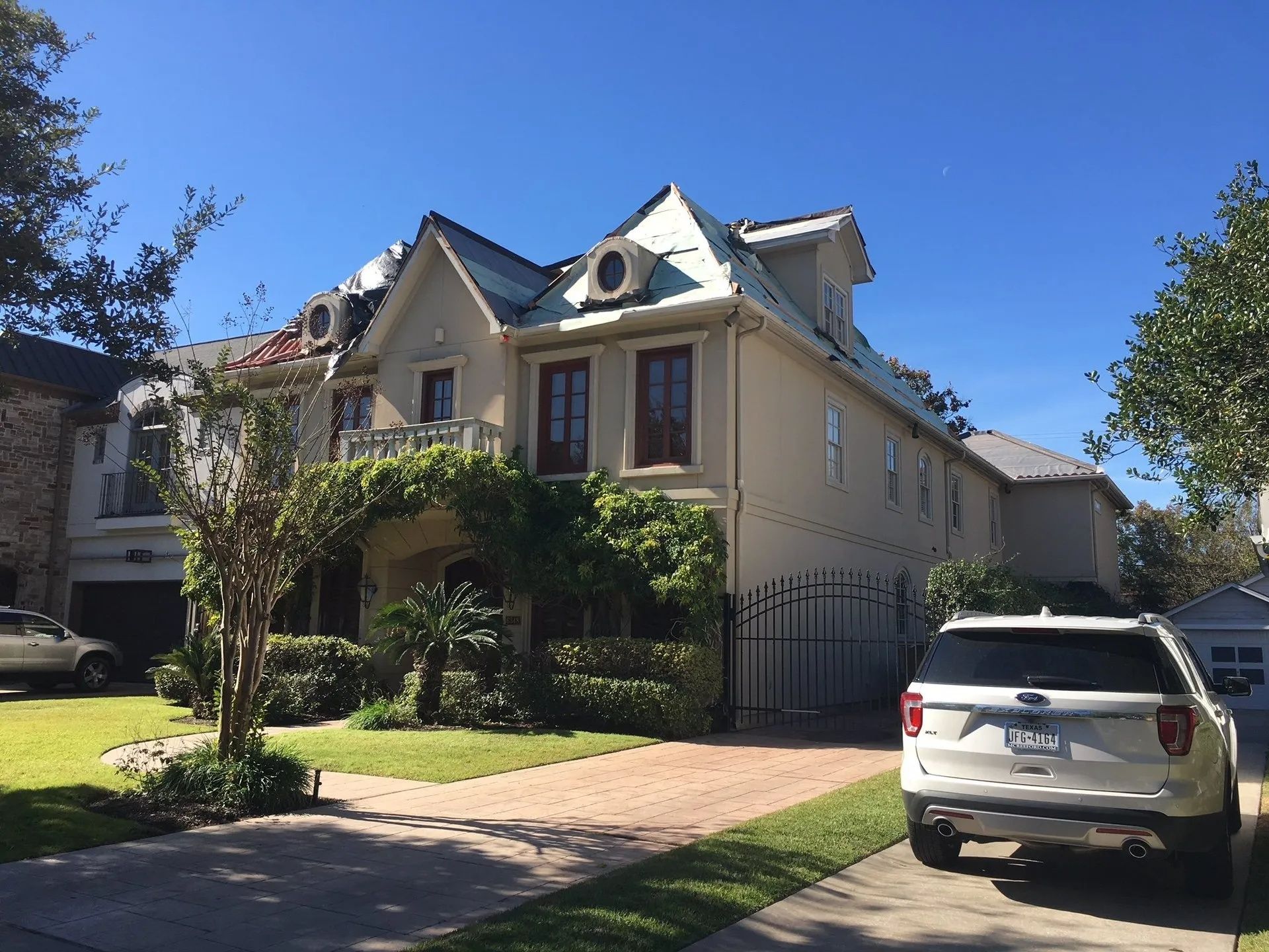 Victorian-style house with a front lawn and driveway, white SUV parked in front under a bright blue sky