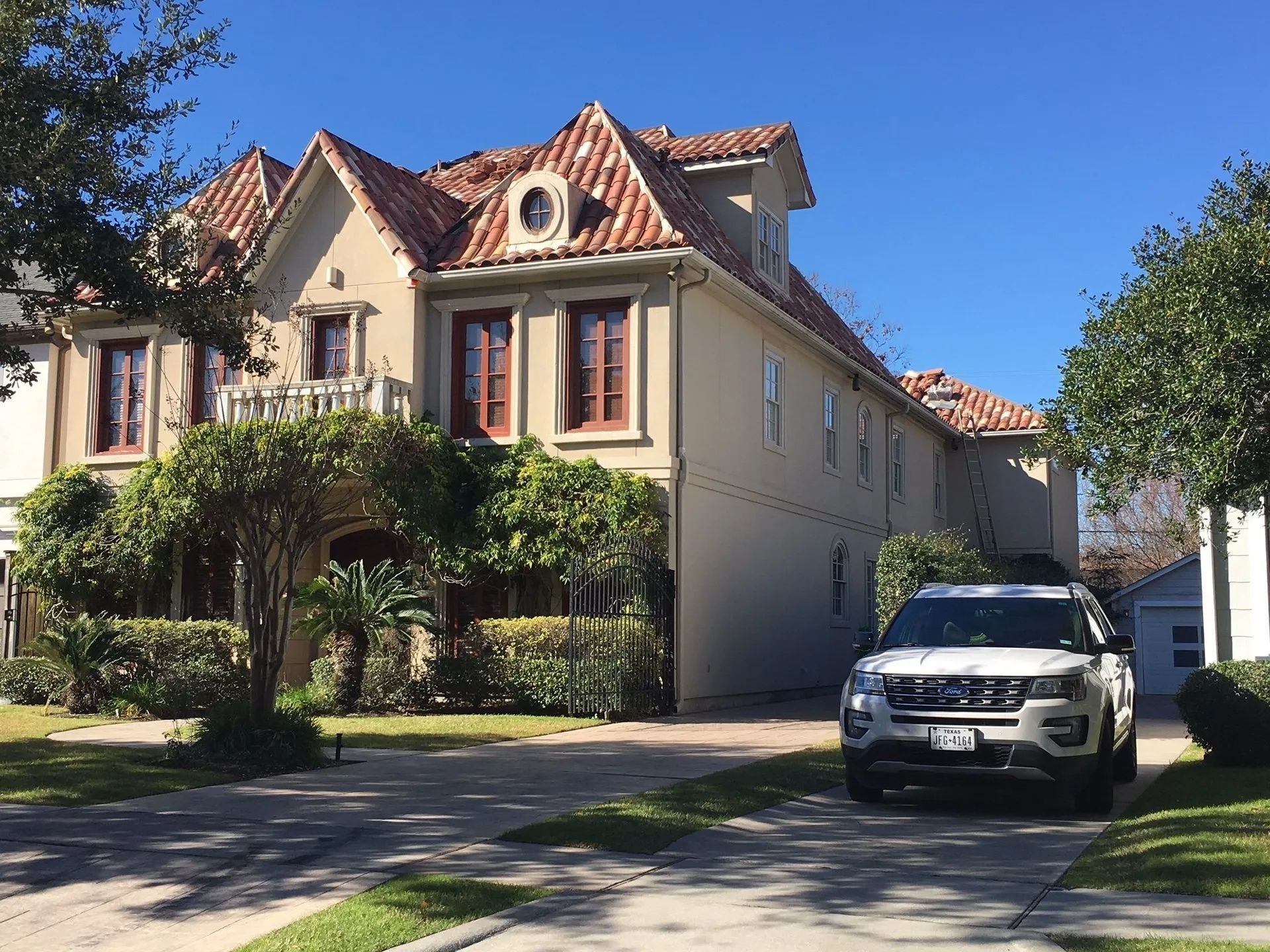 Large stucco house with red-tile roof and ivy-covered porch, with a white SUV parked in the driveway.